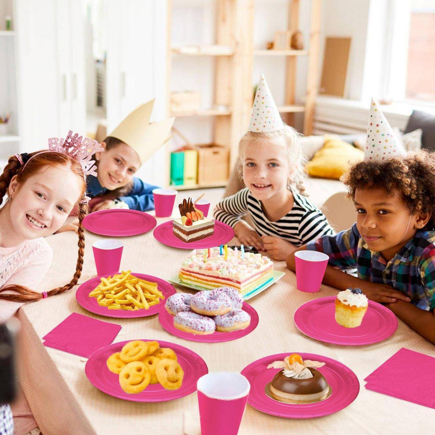 Vier Kinder mit Partyhüten lächeln um einen Tisch bei einer Geburtstagsfeier, mit bunten Kuchen, Donuts, Keksen, Pommes Frites, Bechern und rosa Tellern.