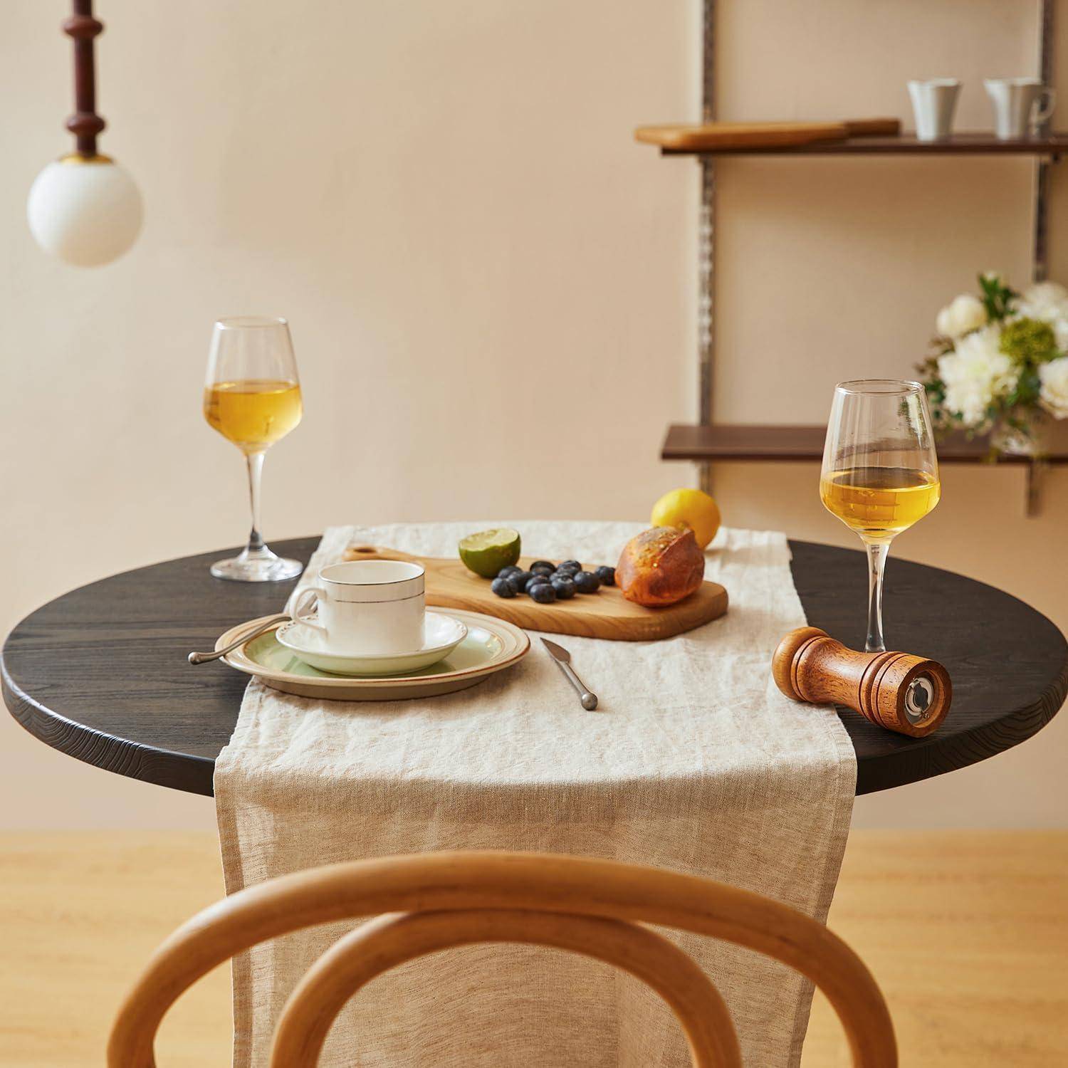 Ein gedeckter Esstisch mit zwei Weingläsern, einer Kaffeetasse mit Untertasse, Obst auf einem Schneidebrett und einer hölzernen Pfeffermühle in einem warmen Zimmer.