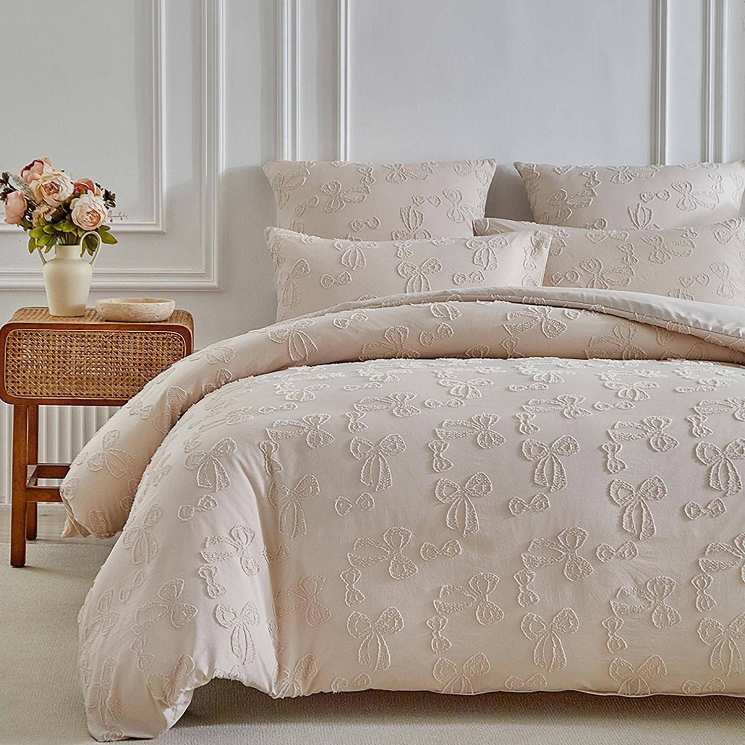 Ein ordentlich gemachtes Bett mit beigefarbener Blumenbettwäsche und Kissen neben einem Nachttisch aus Rattan, auf dem eine Blumenvase und eine Schüssel stehen.