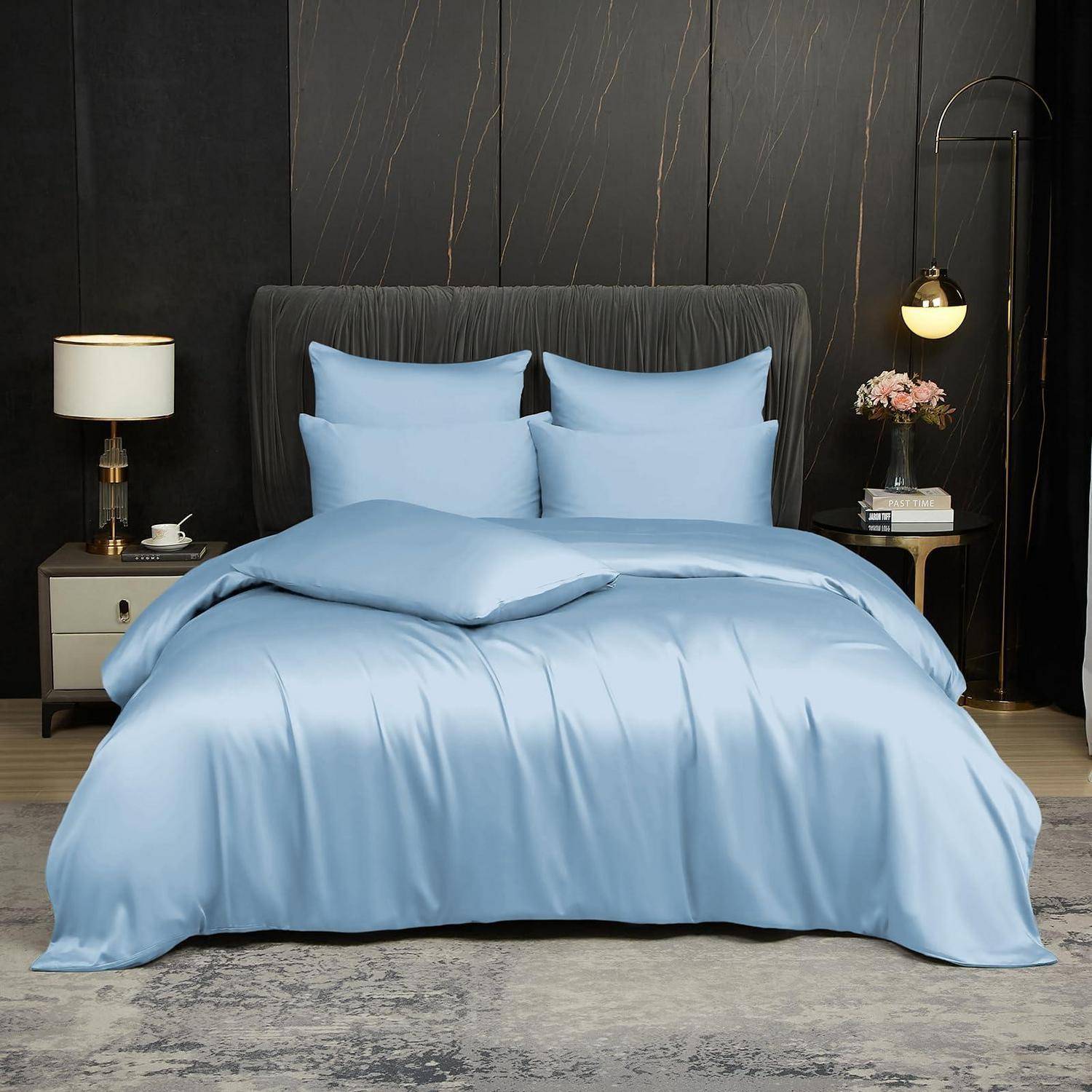 Ein ordentlich gemachtes Bett mit hellblauer Bettwäsche und Kissen in einem modernen dunklen Schlafzimmer, flankiert von Nachttischlampen und Dekoration.