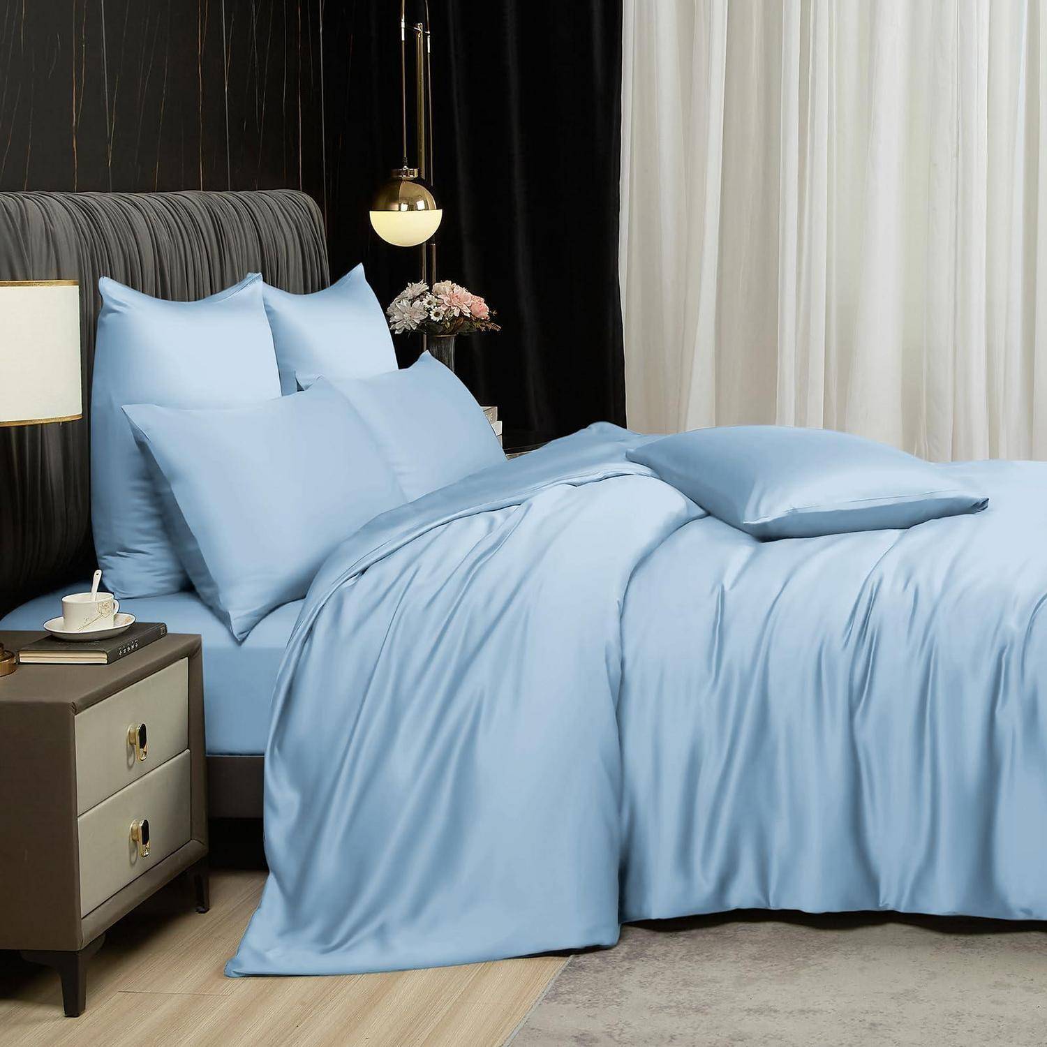 Ein sorgfältig gemachtes Bett mit hellblauer Bettwäsche und Kissen in einem modernen Schlafzimmer neben einem Nachttisch und einer Lampe.