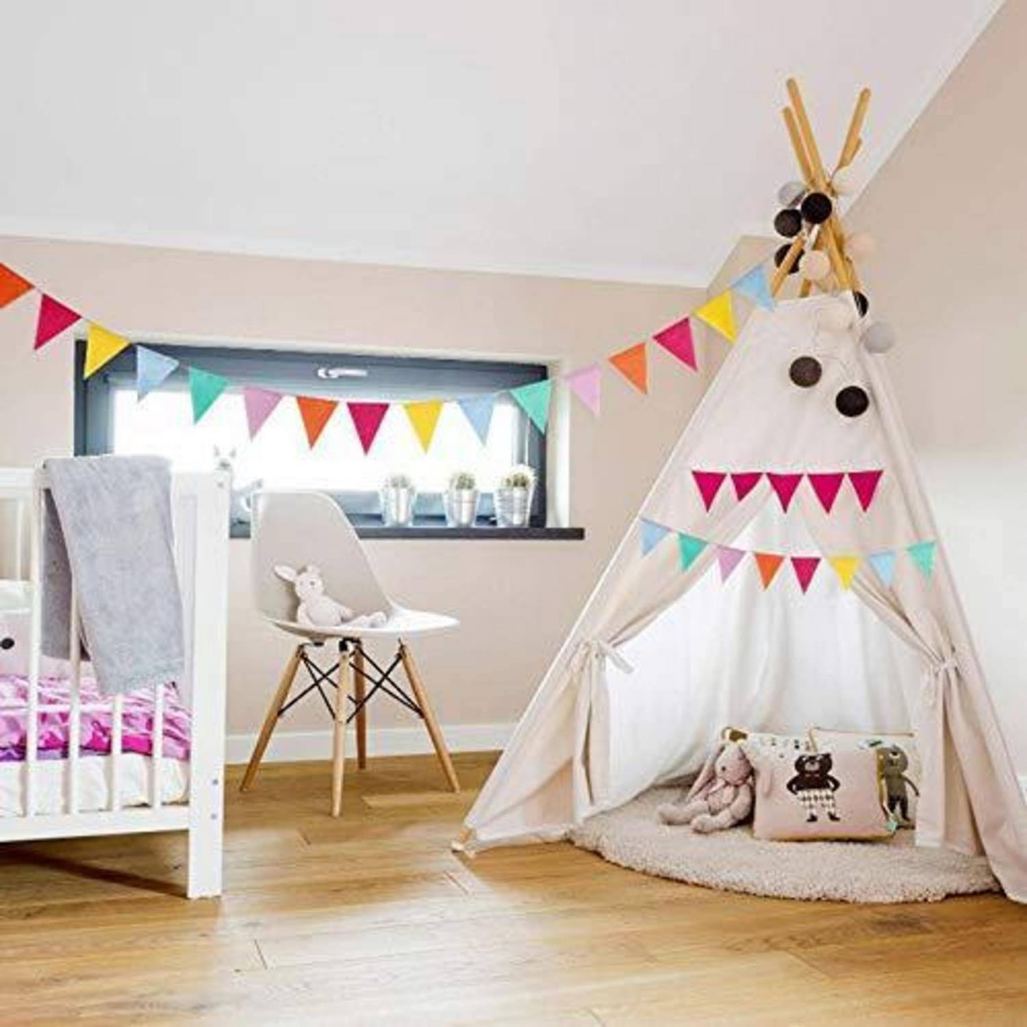 Kinderzimmer mit einer weißen Wiege, einem Stuhl und einem Spieltipi, das mit bunten Wimpeln und Kissen auf einem Holzboden dekoriert ist.