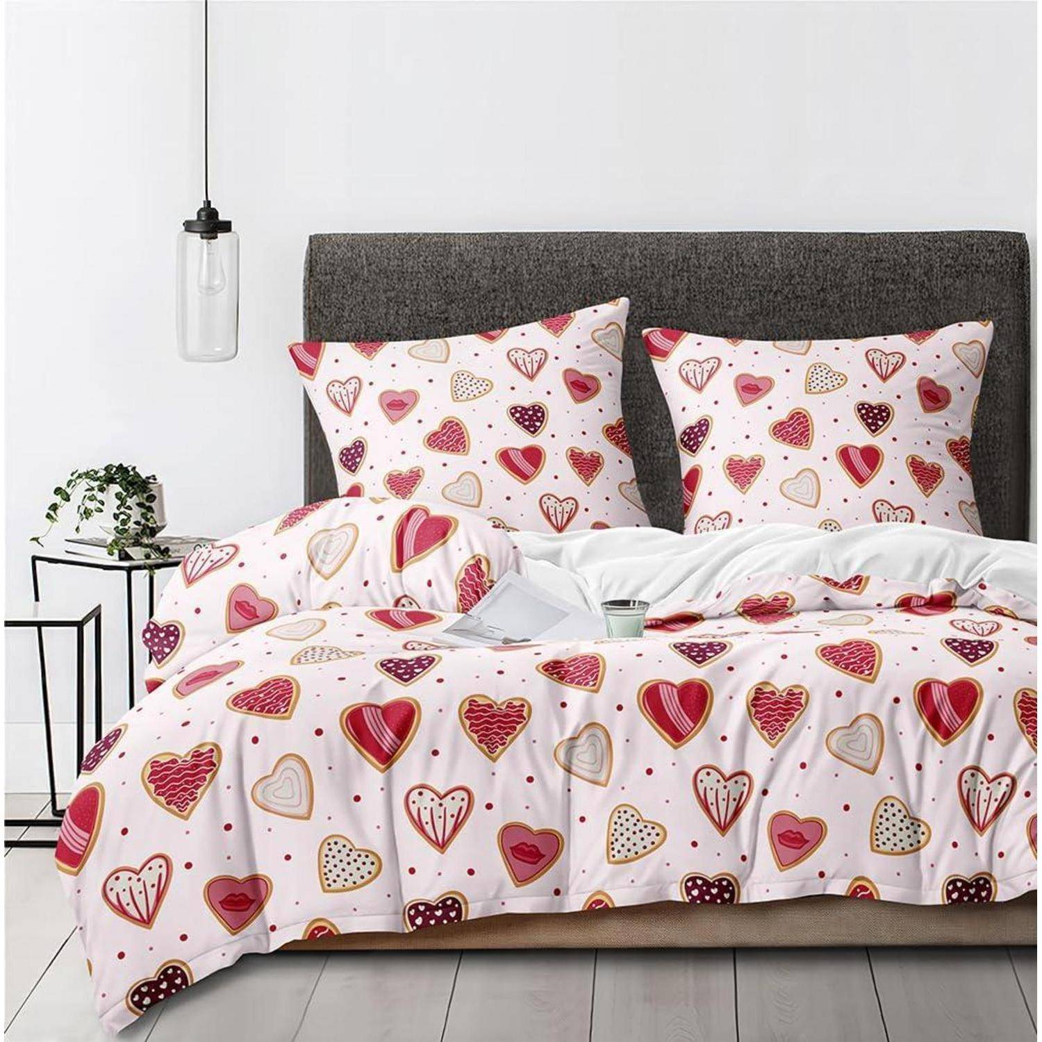 Ein Bett mit rosa Steppdeckenbezug mit Herzenmuster und passenden Kissen, gezeigt in einem minimalistischen Schlafzimmer mit dunkelgrauem Kopfteil und hängender Lampe.