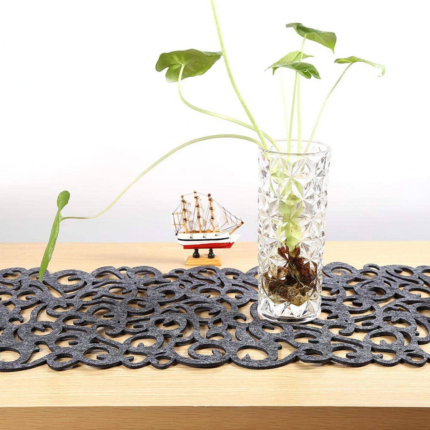 Klare gemusterte Vase mit einer jungen rankenden grünen Pflanze auf einem Holztisch, daneben ein kleines dekoratives Modellschiff.