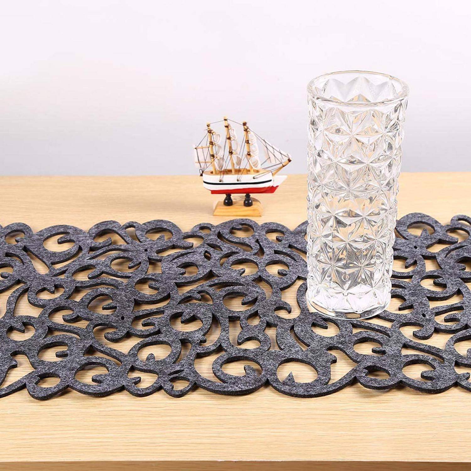 Hohes gemustertes Glas auf einem schwarzen dekorativen Tischläufer, mit einem kleinen Modellsegelboot auf einem Holztisch im Hintergrund.