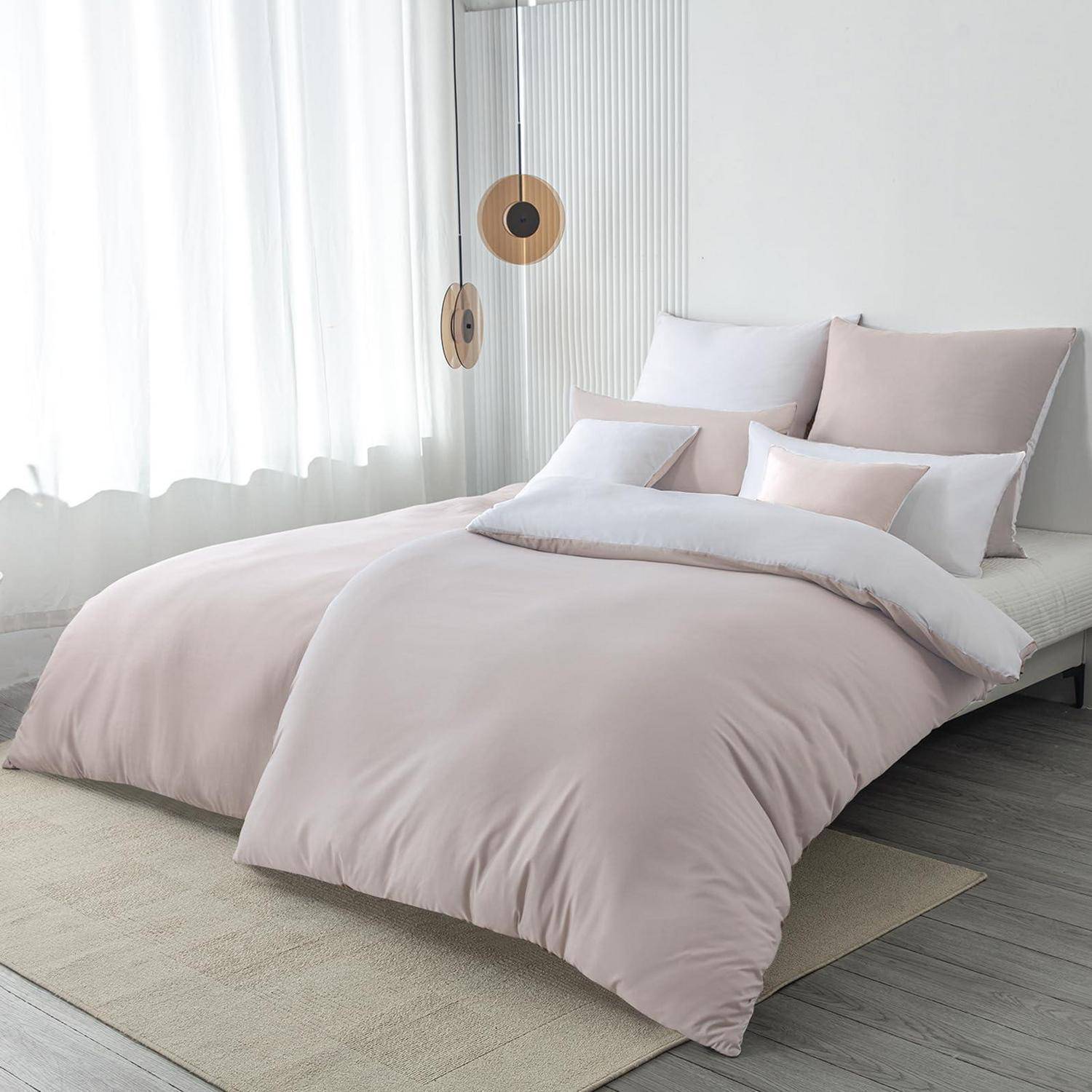 Minimales Schlafzimmer mit einem ordentlich gemachtem Bett in zartem Rosa und weißer Bettwäsche neben transparenten Vorhängen und hängender runder Dekoration.