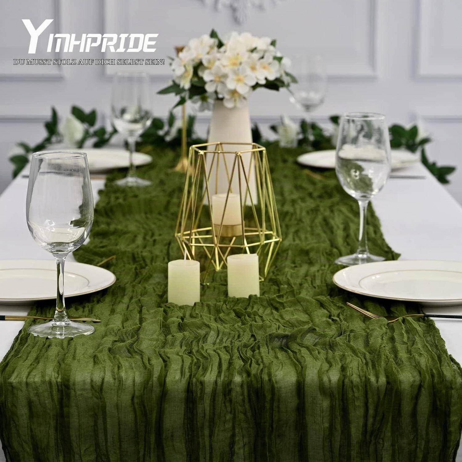 Elegantes Esstisch-Centerpiece mit grünem Rüschenläufer, Kerzen, goldenem Kerzenhalter, weißen Blumen, Tellern und Weingläsern.