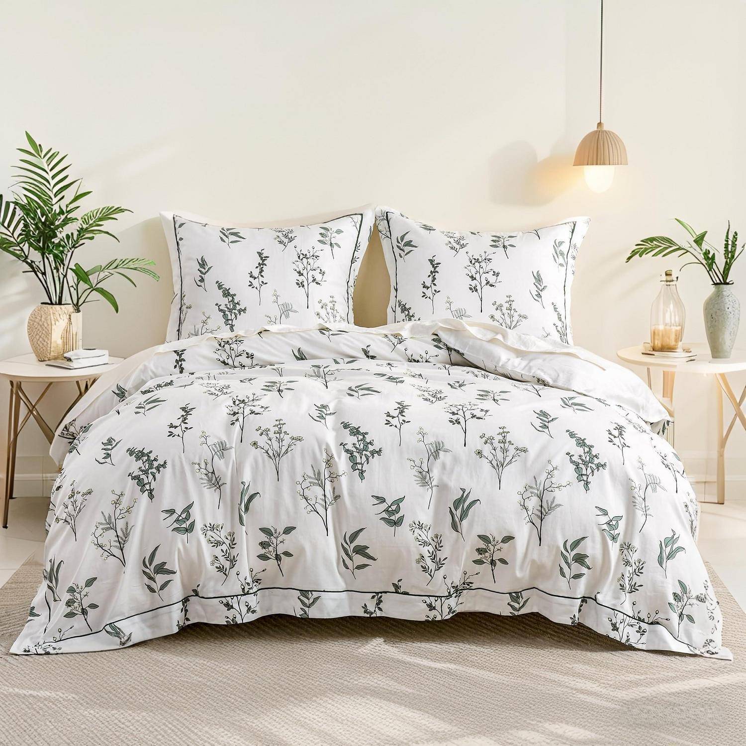 Weißes Bett mit floraler Bettwäsche und passenden Kissen in einem hellen minimalistischen Schlafzimmer, flankiert von kleinen Nachttischen und Pflanzen.
