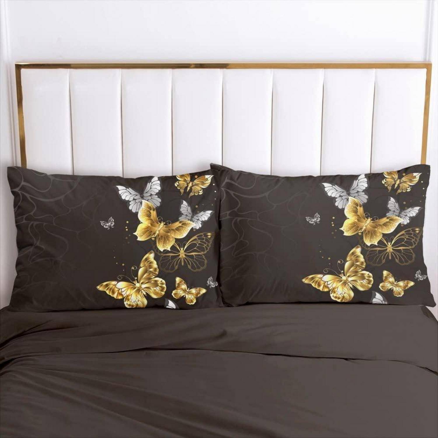 Ein sorgfältig gemachtes Bett mit dunkelbrauner Bettwäsche und passenden Kissen mit Schmetterlingsdruck vor einem weiß gepolsterten Kopfteil.