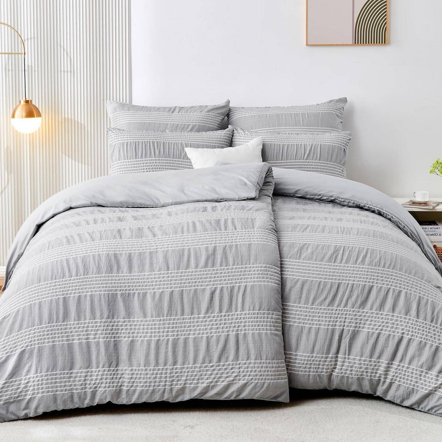 Ein ordentlich gemachtes Bett mit hellgrauem gestreiftem Bettzeug und Kissen in einem hellen minimalistischen Schlafzimmer.