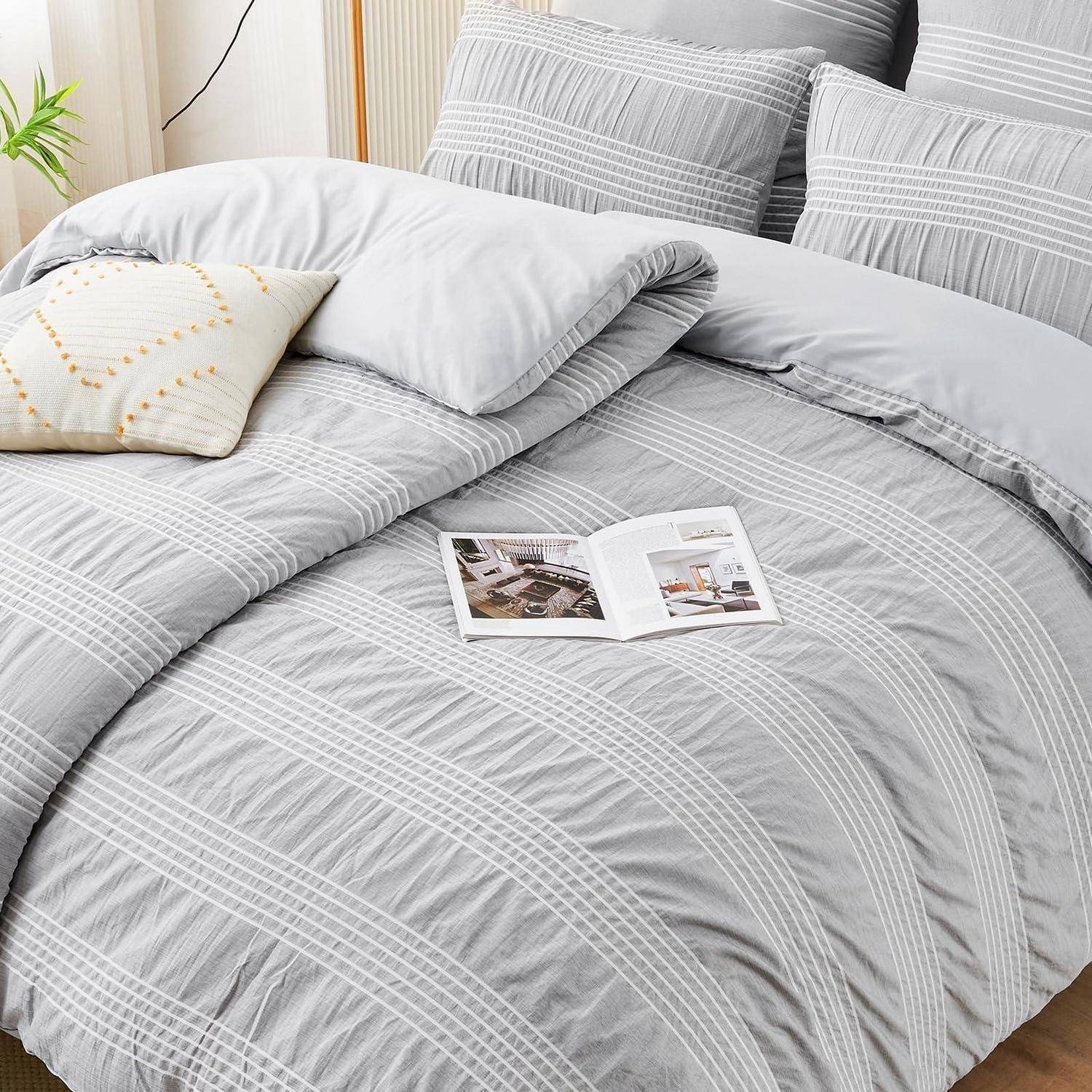 Grau gestreiftes Bettwäsche-Set auf einem gemachten Bett mit Kissen und einer offenen Zeitschrift, die ein ordentliches modernes Schlafzimmer zeigt.
