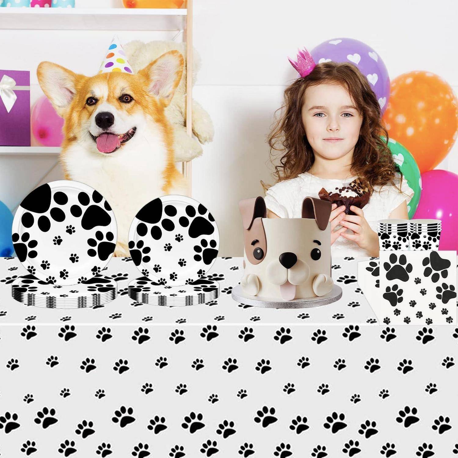 Ein Corgi mit einer Partyhut und ein junges Mädchen sitzen hinter einem mit Pfotenbdrucken dekorierten Geburtstagstisch mit einem hundegestaltigen Kuchen, Tellern, Boxen und Luftballons.