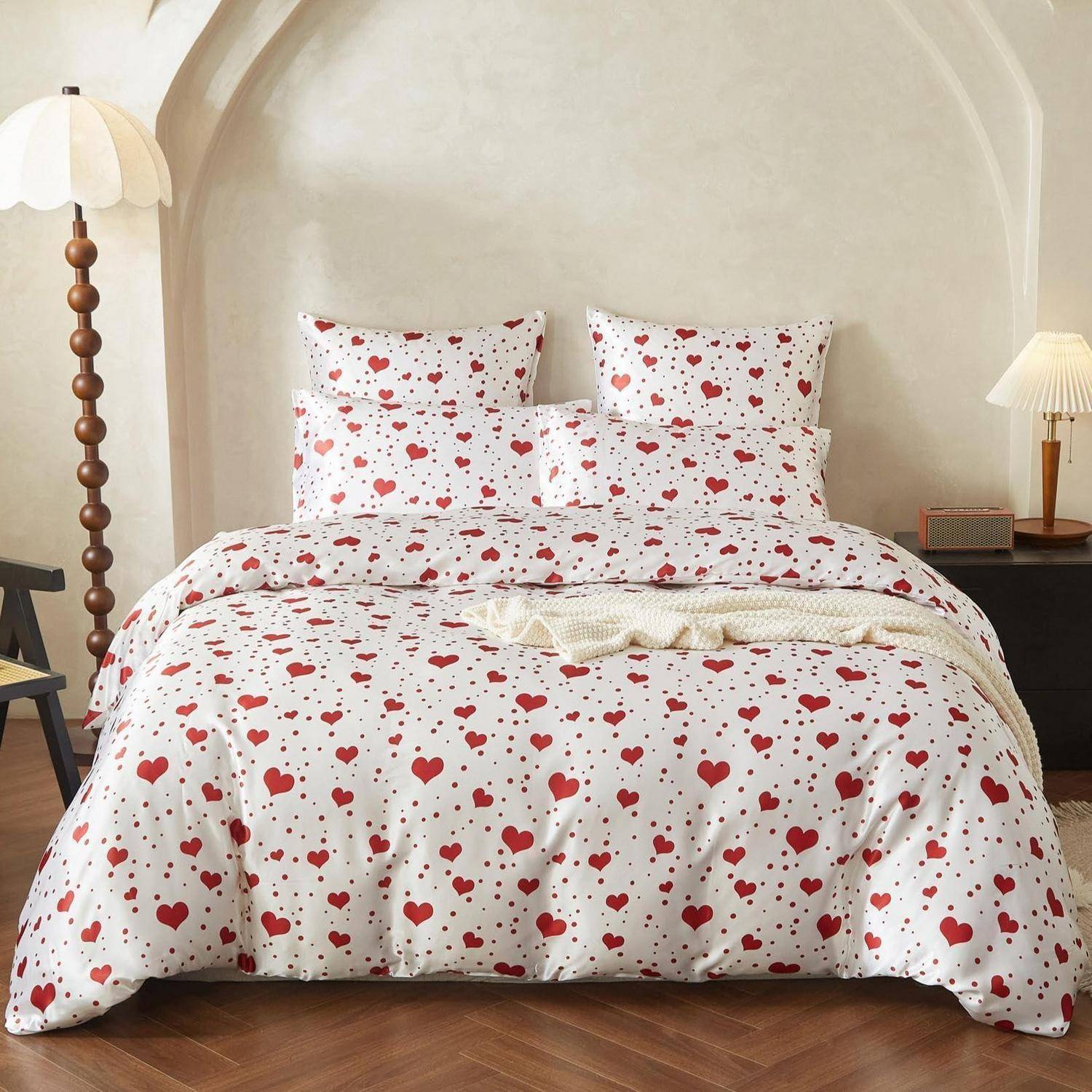 Schlafzimmer mit einem ordentlich gemachten Bett, das mit weißer Bettwäsche mit roten Herzmustern bezogen ist, passenden Kissen und einer beigen gewölbten Wand dahinter.
