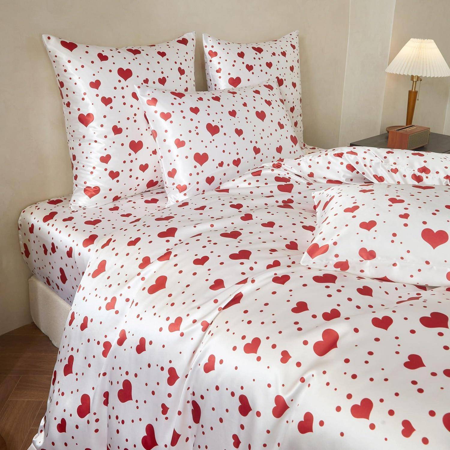 Bett mit weißer Bettwäsche, die mit einem roten Herzmuster bedeckt ist, einschließlich passender Kissen und Bettdecke in einem Schlafzimmer.