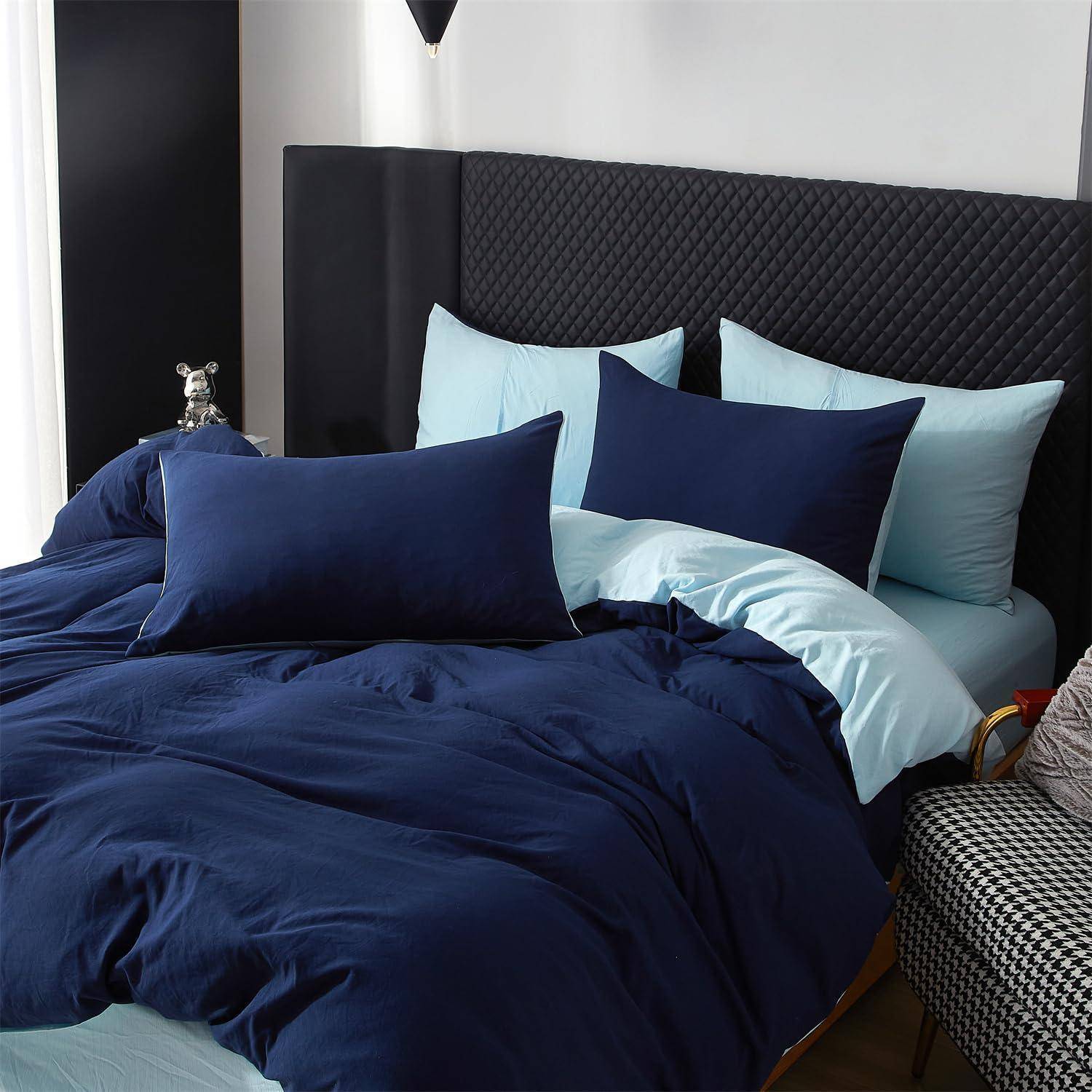 Ordentlich gemachtes Bett mit dunkelblauer und hellblauer Bettwäsche und mehreren Kissen vor einem schwarz gepolsterten Kopfteil in einem modernen Schlafzimmer.