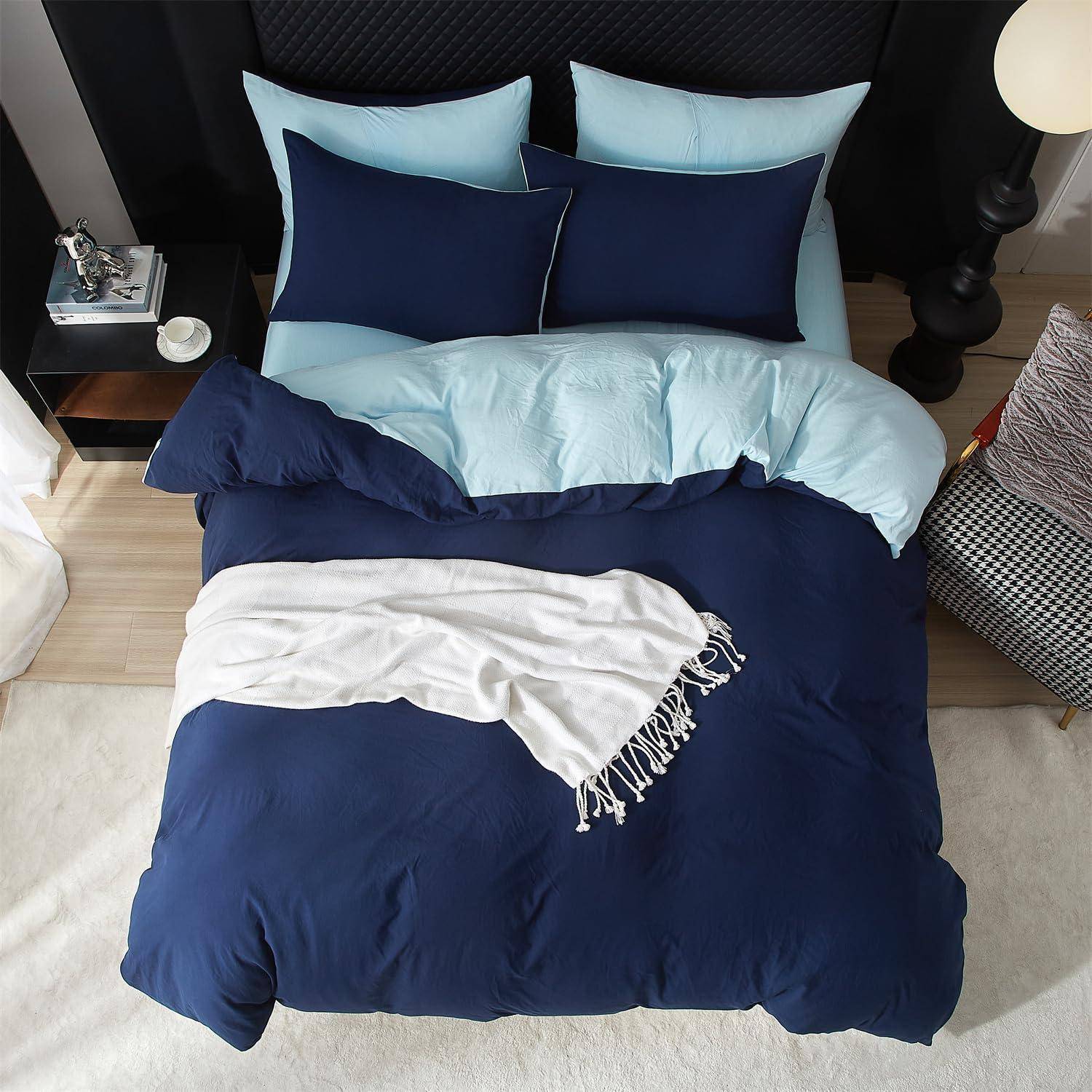 Eine Draufsicht auf ein ordentlich gemachtes Bett mit dunkelblauer und hellblauer Bettwäsche, Kissen und einer weißen Wurfdecke in einem modernen Schlafzimmer.