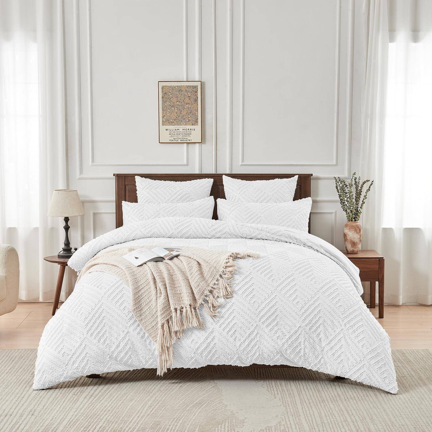Ein ordentlich gemachtes Bett mit weißer strukturierter Bettwäsche und Kissen, eine beigefarbene Wurf­decke und passende Nachttische in einem hellen, minimalistischen Schlafzimmer.