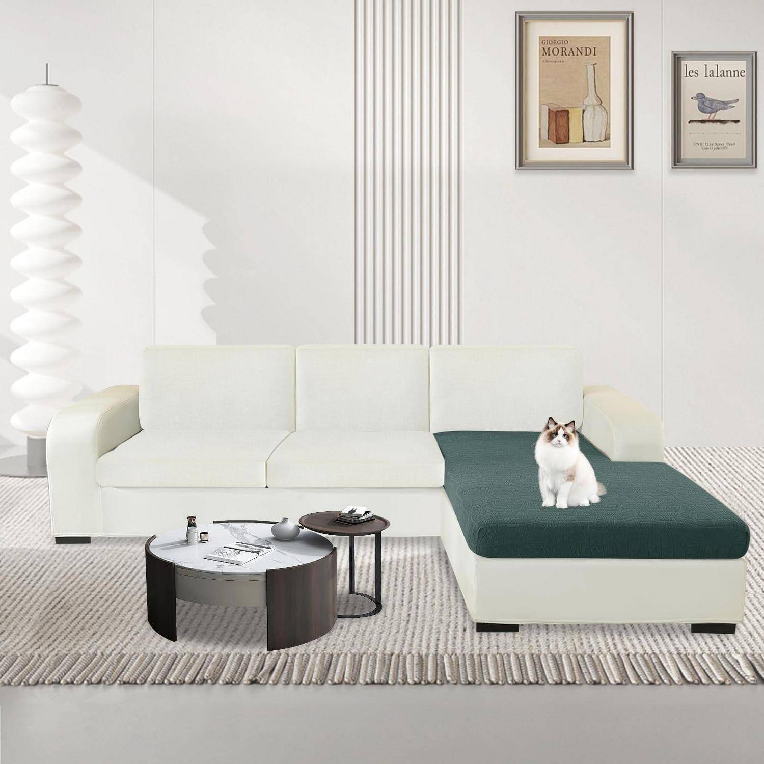 Modernes Wohnzimmer mit weißem Ecksofa, dunkelgrüner Chaiselongue, Couchtischen, Wandkunst und einer Katze, die auf der Chaiselongue sitzt.