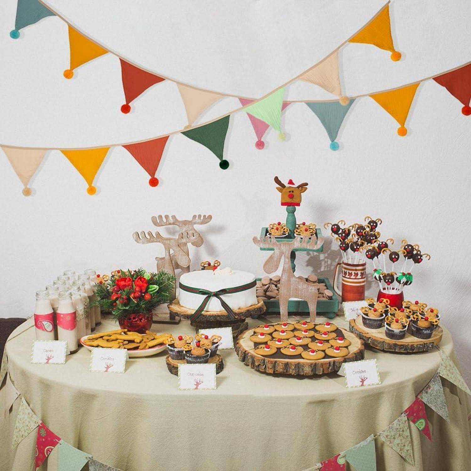 Festliche Desserttafel mit rentierförmigen Kuchenständern, Keksen, Cupcakes und Süßigkeiten, dekoriert mit bunten Wimpelketten für eine Weihnachtsfeier.