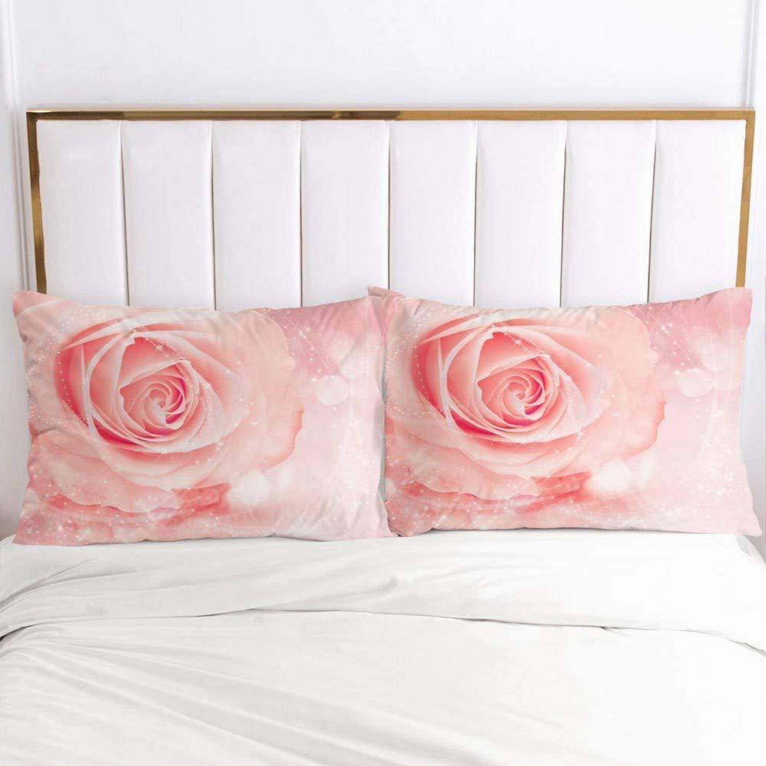 Ein Bett mit zwei rosa rosenmusterten Kissen gegen ein weiß gepolstertes Kopfteil und weiße Bettwäsche.