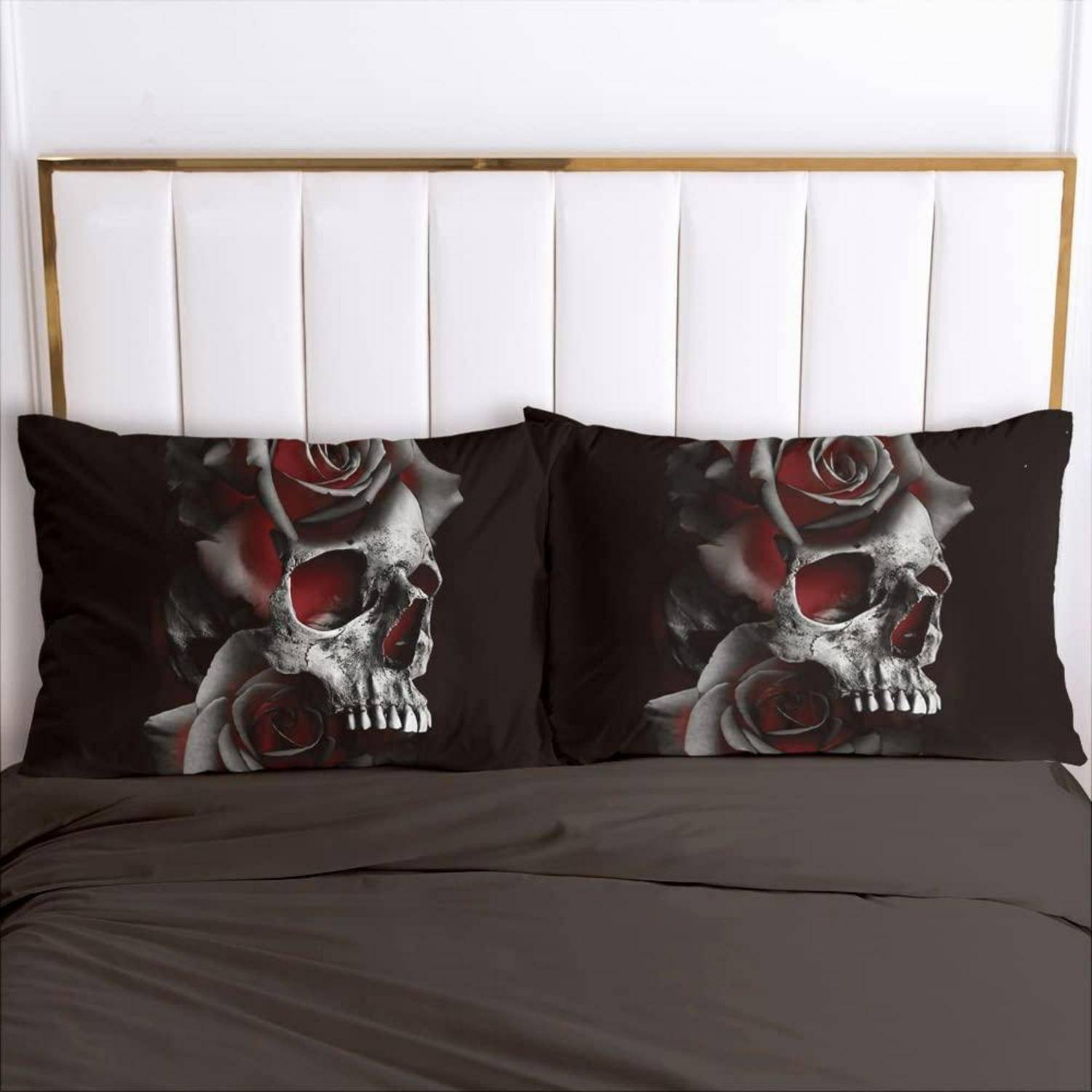 Ein Bett mit dunkelgrauer Bettwäsche und zwei passenden schwarzen Kissenbezügen mit einem Schädel- und rote Rosen-Design auf weißem Kopfteil.