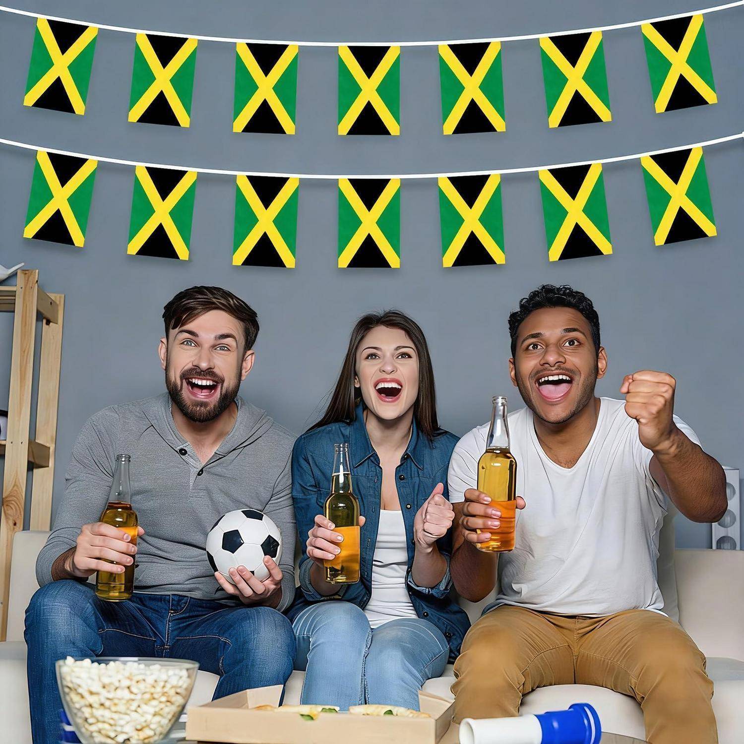 Drei Freunde auf einem Sofa jubeln mit Getränken und einem Fußball vor jamaikanischen Flaggen, während sie ein Sportspiel anschauen.