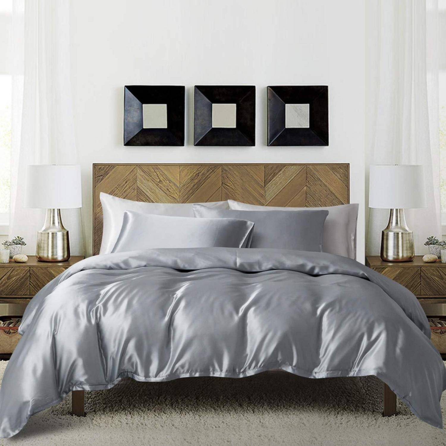 Modernes Schlafzimmer mit einem ordentlich gemachtem Bett, grauer Bettwäsche, hölzernem Kopfteil, passenden Nachttischlampen und drei quadratischen Wandkunstwerken darüber.