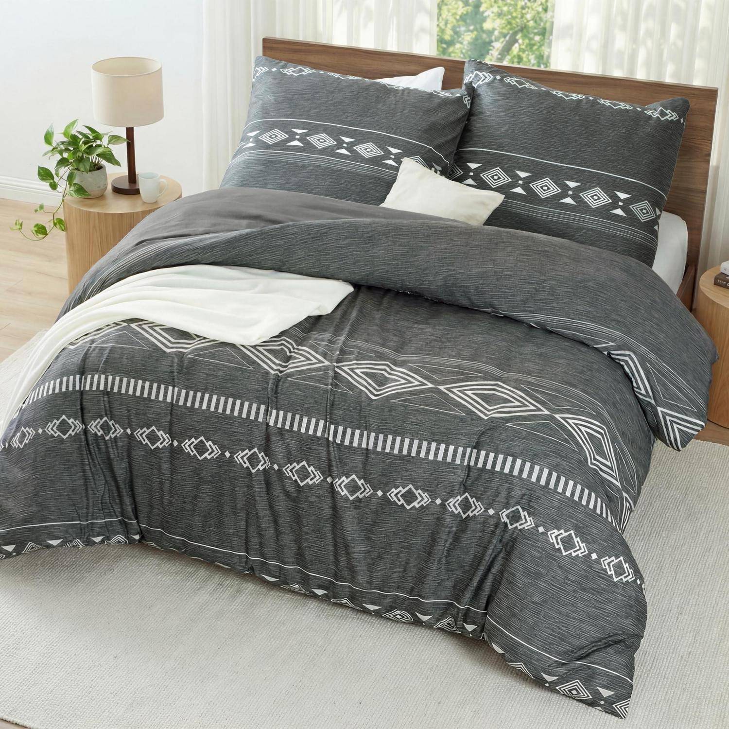Grau gemustertes Bettwäscheset auf einem gemachten Bett mit weißen Laken und Kissen in einem hellen Schlafzimmer.