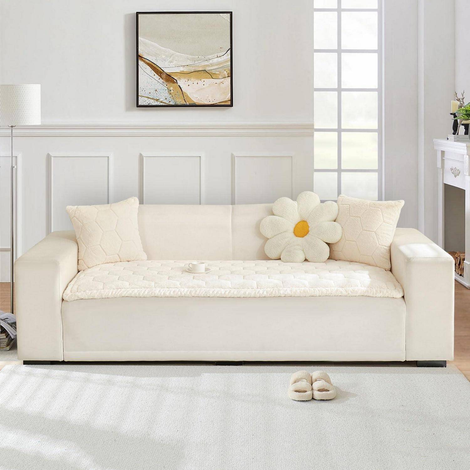 Cremefarbenes Sofa mit gestepptem Bezug und Blumenkissen in einem hellen Wohnzimmer, dargestellt mit passenden Kissen, Hausschuhen, Stehleuchte und Wandkunst.