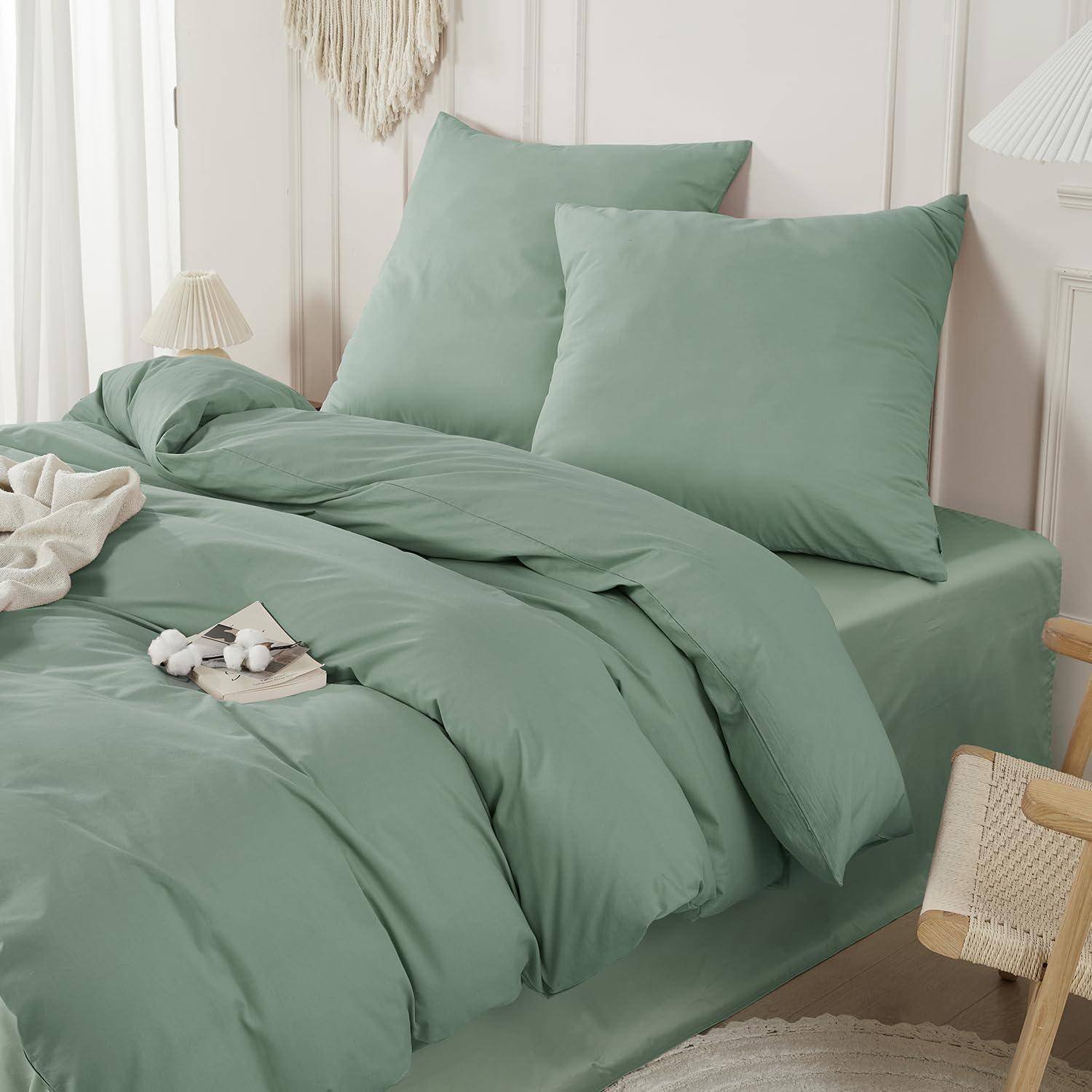Ein ordentlich gemachtes Bett mit salbeigrünem Bettdeckenbezug und passenden Kissen in einem hellen, gemütlichen Schlafzimmer.