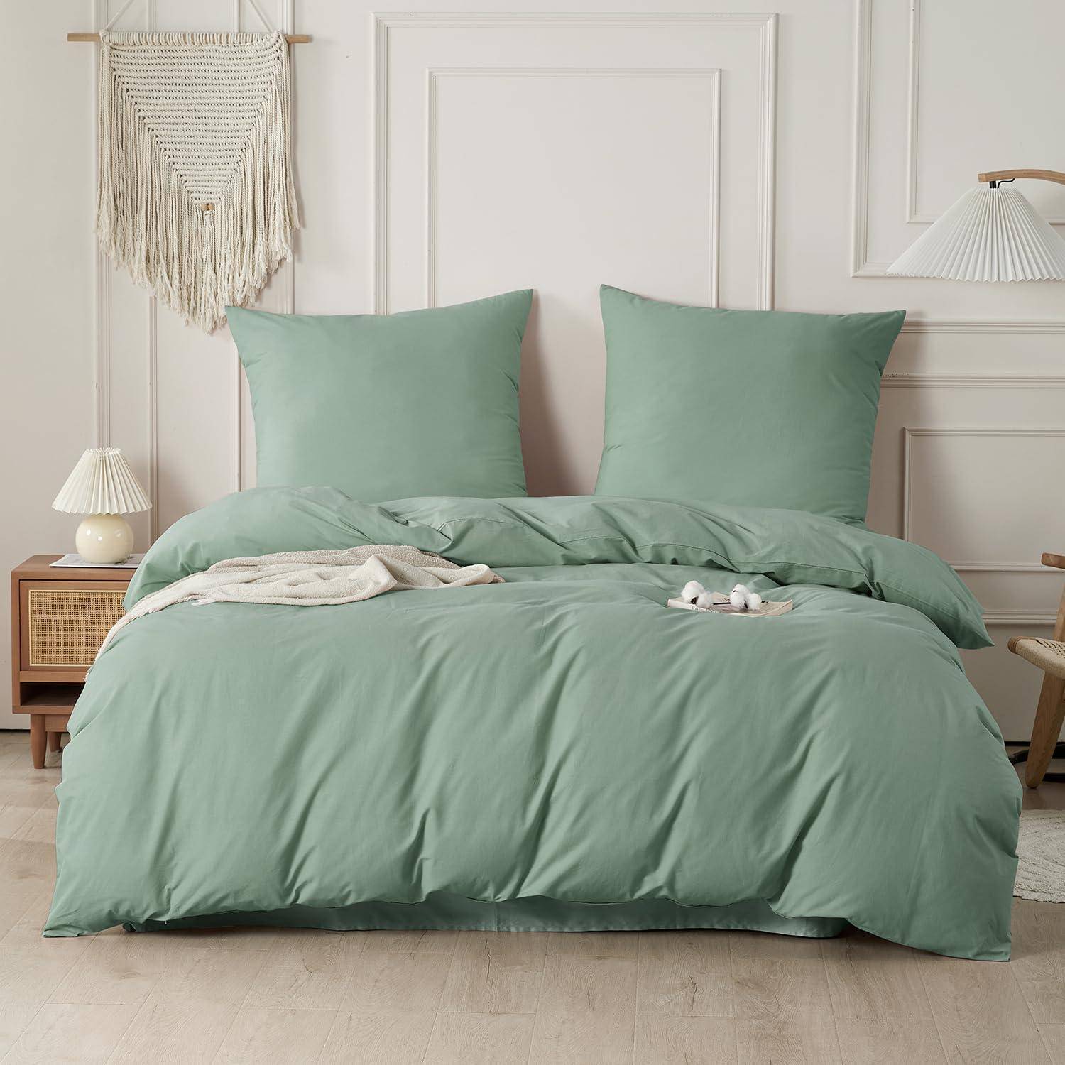 Ordentlich gemachtes Bett mit graugrüner Bettwäsche und zwei Kissen in einem hellen, minimalistischen Schlafzimmer.