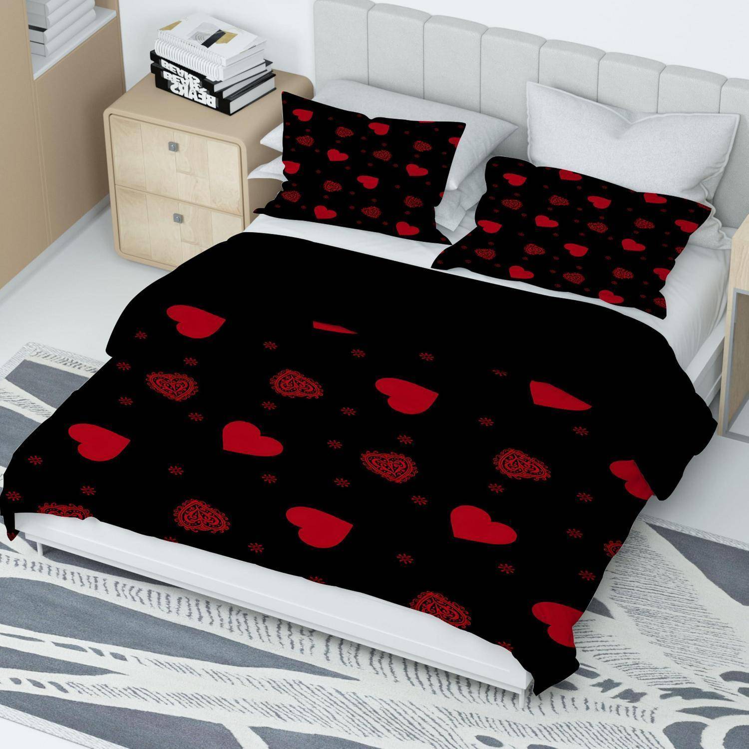 Schlafzimmer mit einem weißen Bett, das mit schwarzer Bettwäsche mit roten Herzmustern bezogen ist und passenden Kissen, neben einem kleinen Nachttisch mit gestapelten Büchern.