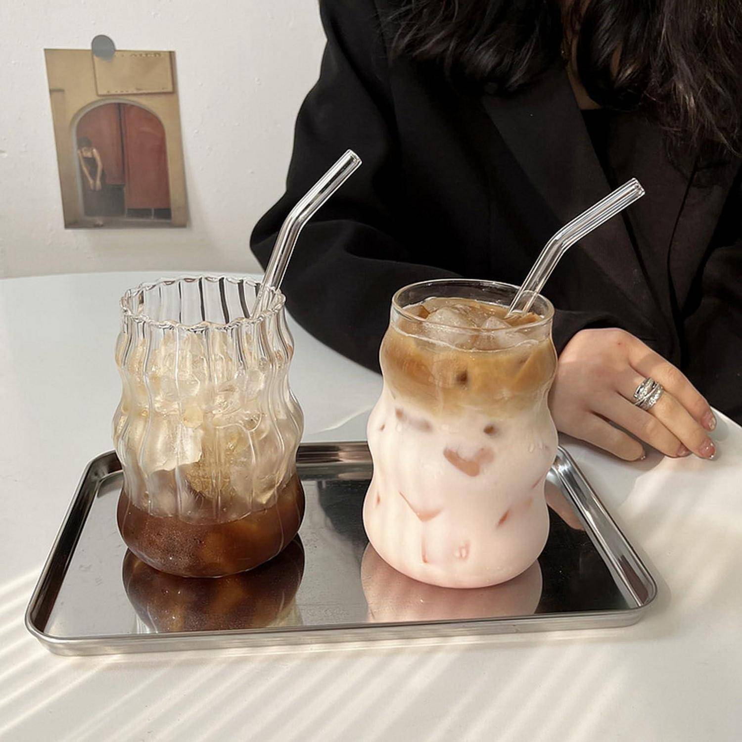 Zwei eisgekühlte geschichtete Getränke in Glastassen auf einem Metalltablett, ein dunkler Kaffee und ein rosafarbener Latte, neben einer sitzenden Person.