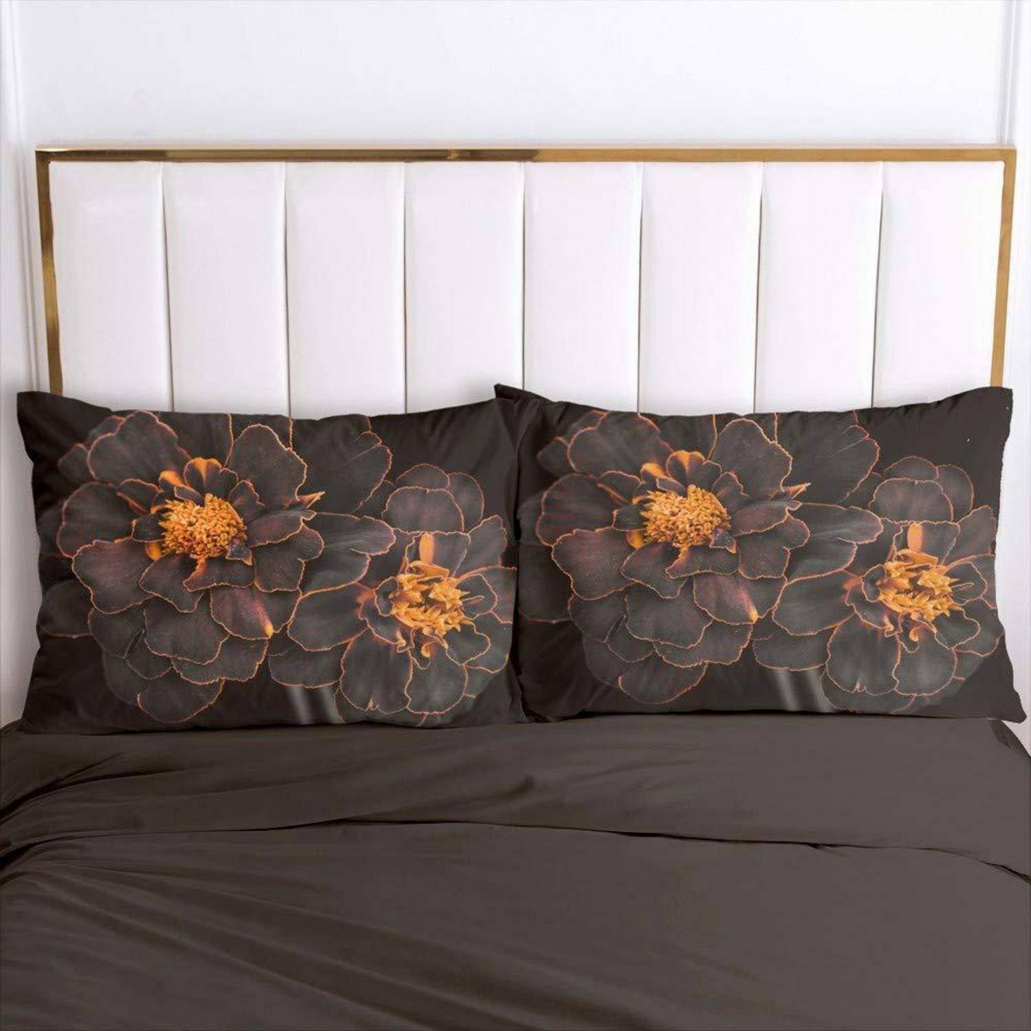 Bett mit weiß gepolstertem Kopfteil und dunkler Bettwäsche, akzentuiert durch zwei schwarze Blumenkissen mit orangefarbenen Blumendesigns.