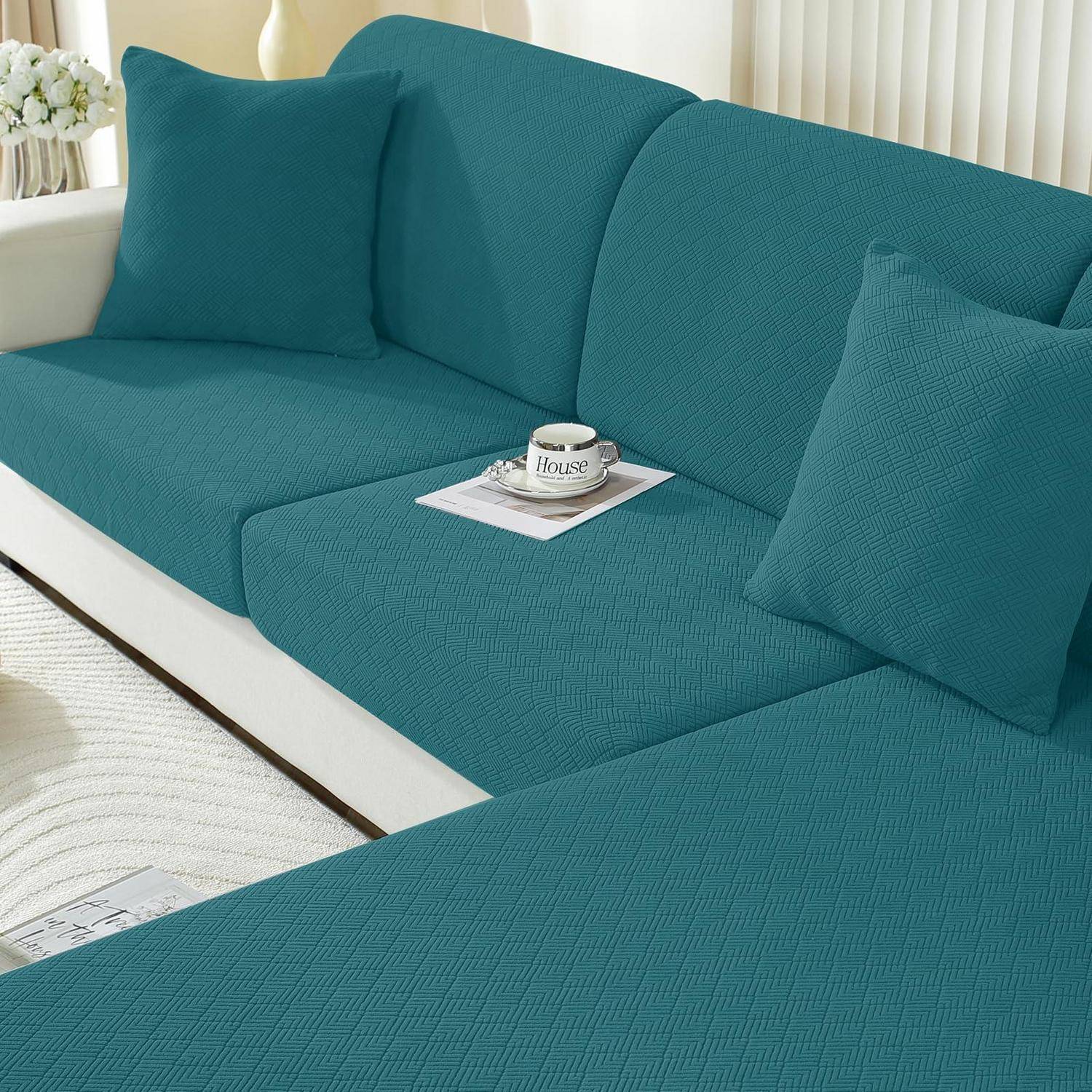 Teerfarbiges Sofa mit Schonbezug in einem hellen Wohnzimmer, mit passenden Dekokissen und einer Kaffeetasse auf einem Tablett.