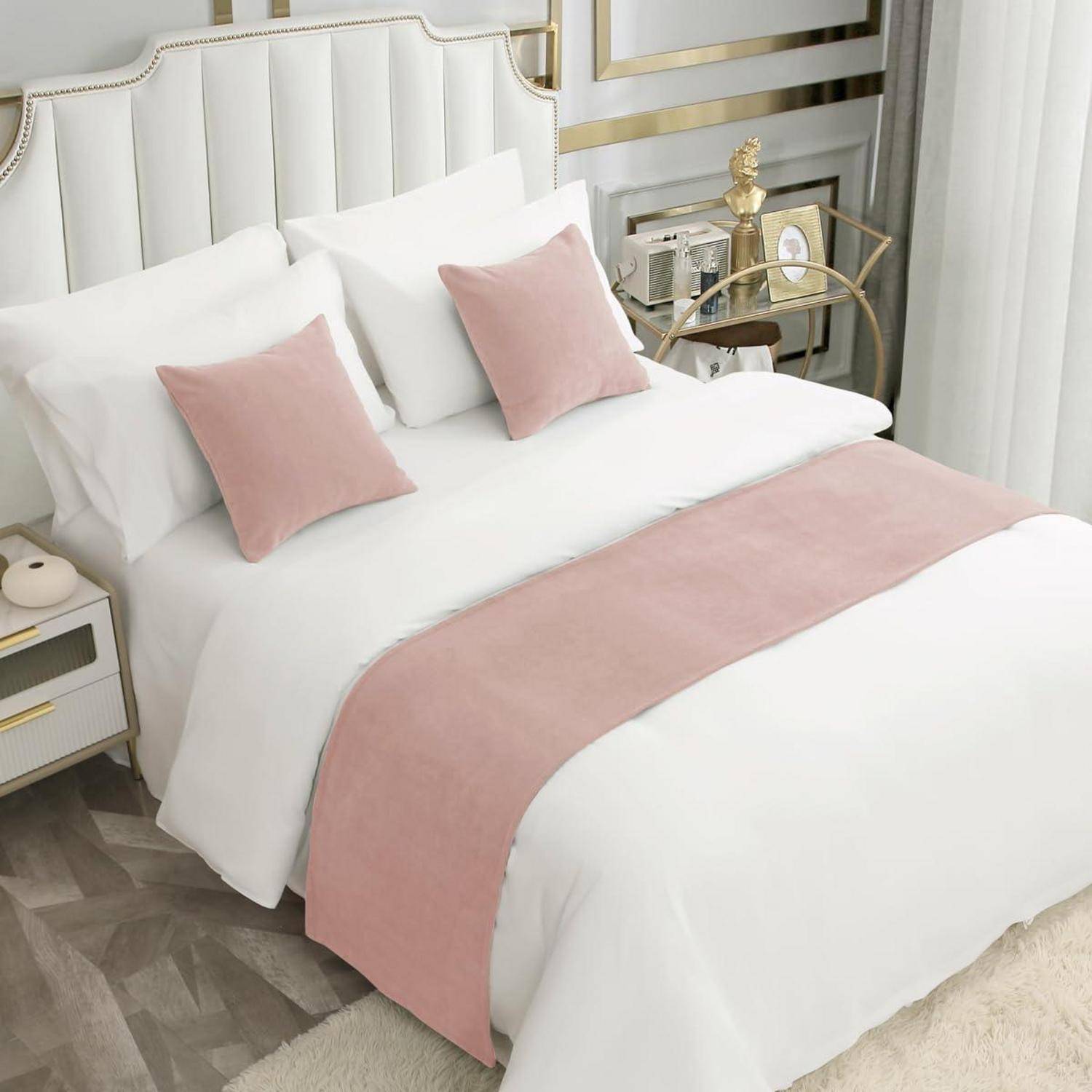 Elegantes Schlafzimmer mit einem weiß gepolsterten Bett, rosa Kissen und einem rosa Bettläufer neben goldfarbenem Dekor.