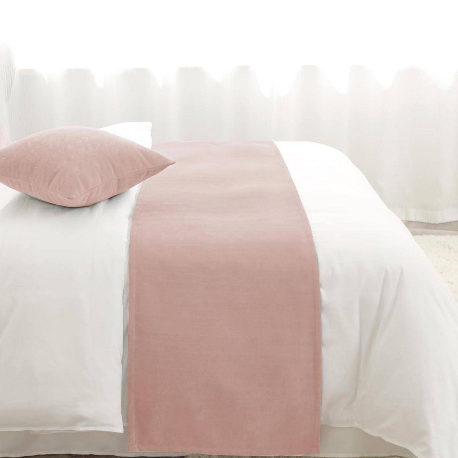 Ordentlich gemachtes Bett mit weißer Bettwäsche und einem zartrosa Kissen und Läufer in einem hellen, minimalistischen Schlafzimmer.