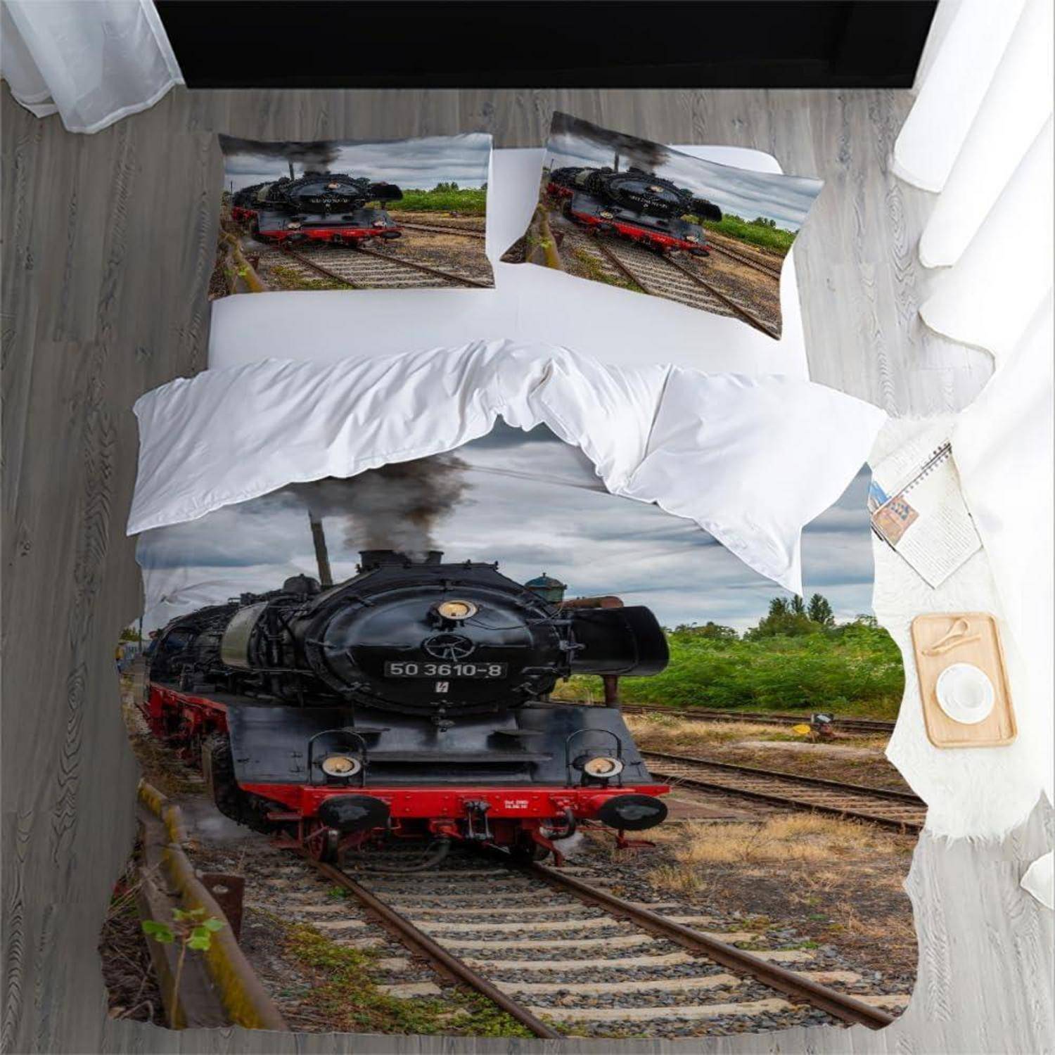 Zuggethema-Bett mit einer schwarzen Dampflokomotive, die auf der Bettwäsche, dem Kissen und der Wandkunst in einem Schlafzimmer mit weißen Vorhängen und grauem Holzboden gedruckt ist.