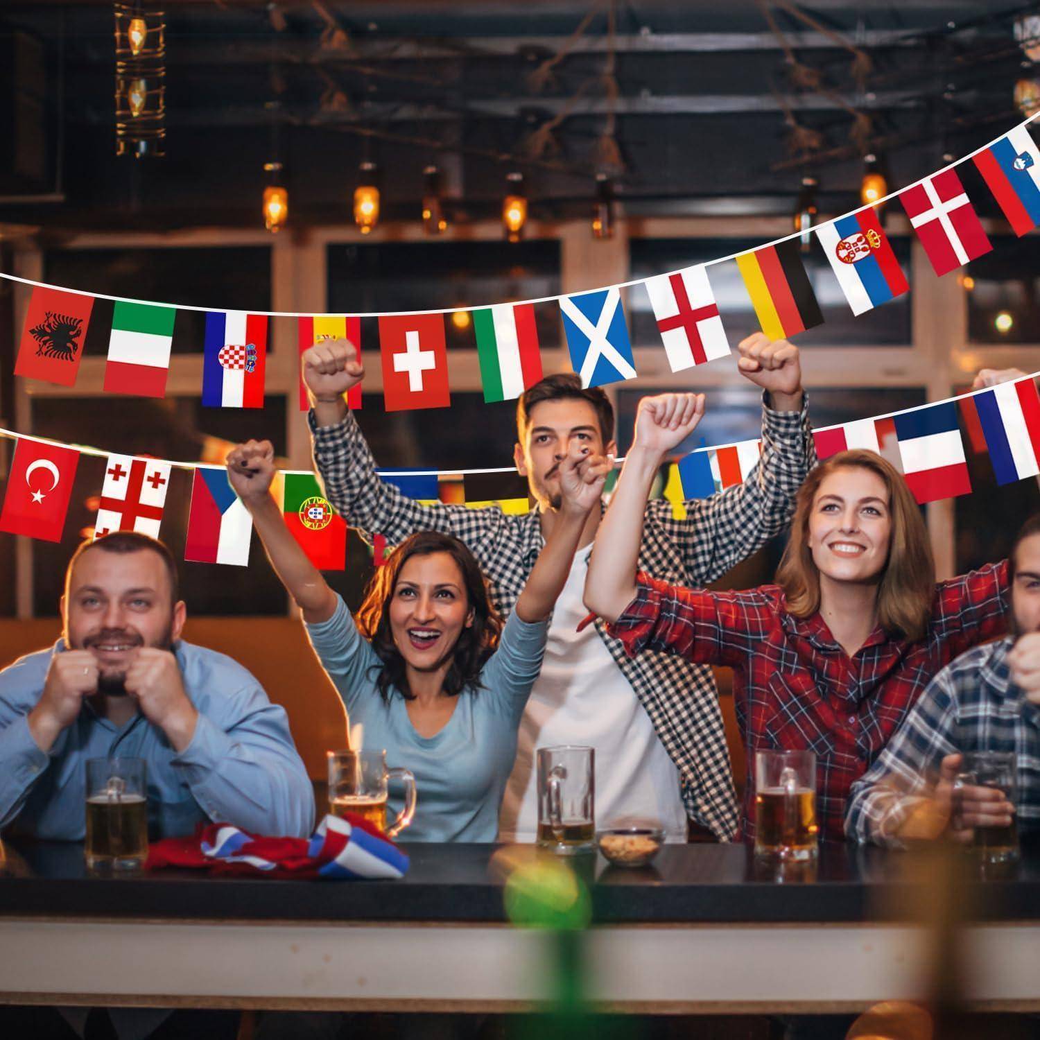 Jubelnd feiernde Freunde in einer Bar erheben ihre Fäuste, während sie ein Sportevent beobachten, umgeben von Girlanden mit internationalen Flaggen.
