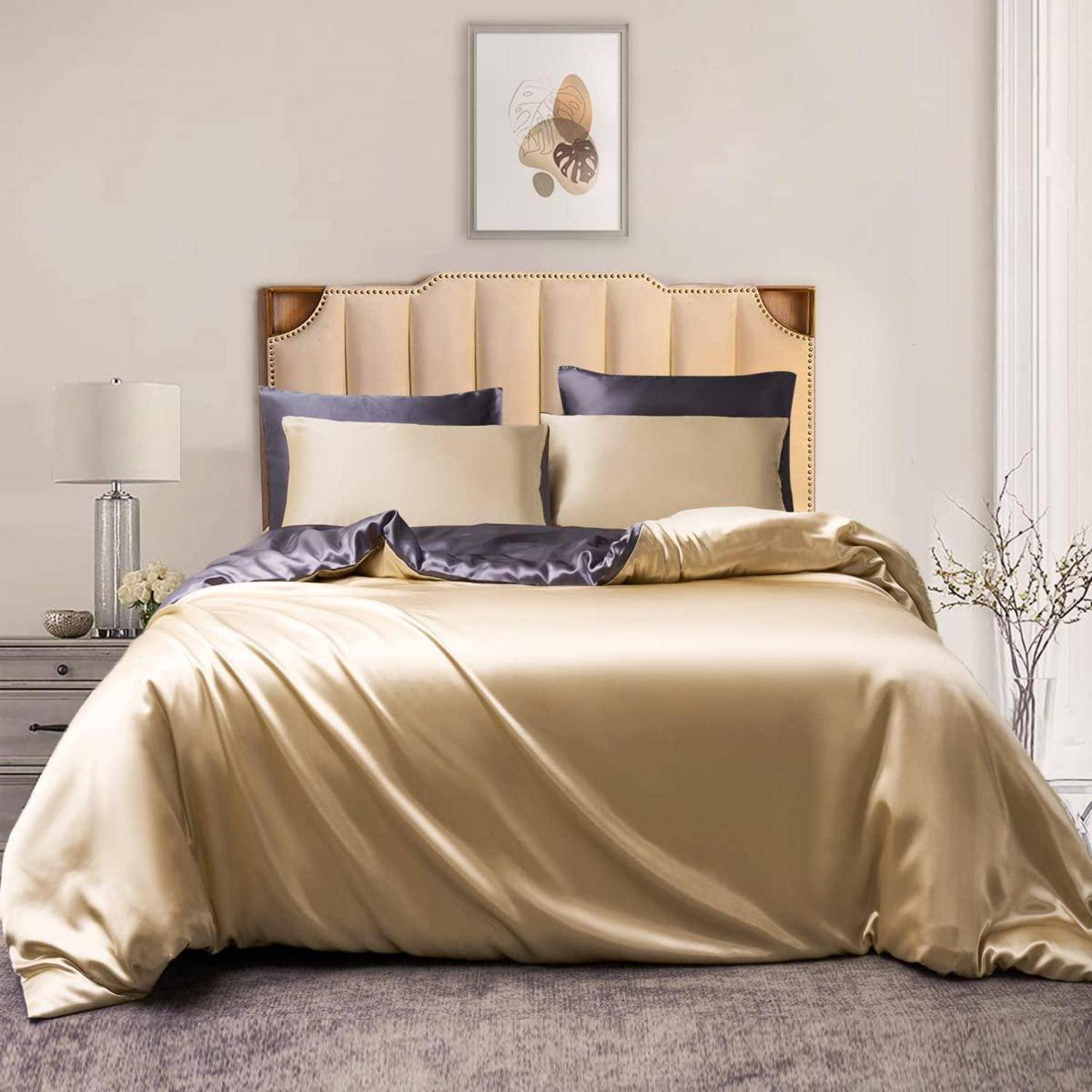 Elegantes Schlafzimmer mit einem ordentlich gemachten Bett, beigefarbener Satinbettwäsche, gepolstertem Kopfteil, Nachttischlampe und gerahmter Wandkunst.