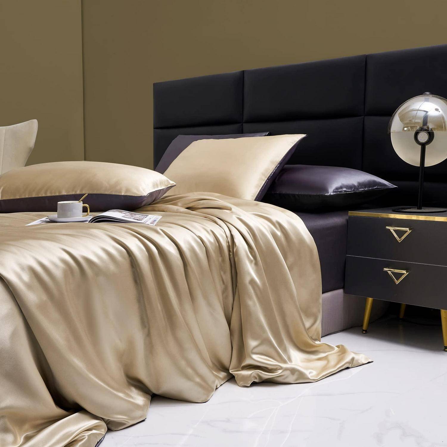 Stilvolles Schlafzimmer mit einem schwarz gepolsterten Bett, beigefarbener Satinbettwäsche und einem schwarzen Nachttisch mit einer Lampe.