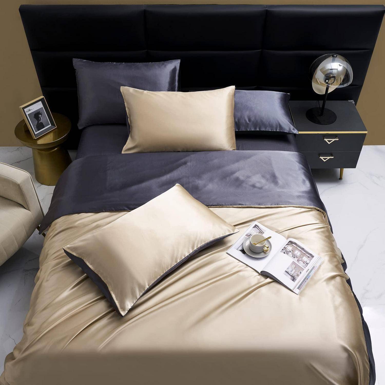 Modernes Bett mit schwarzem Kopfteil, grau- und champagnerfarbener Satinbettwäsche, Kissen und einem Nachttisch mit Lampe und Foto in Rahmen in einem zeitgenössischen Schlafzimmer.