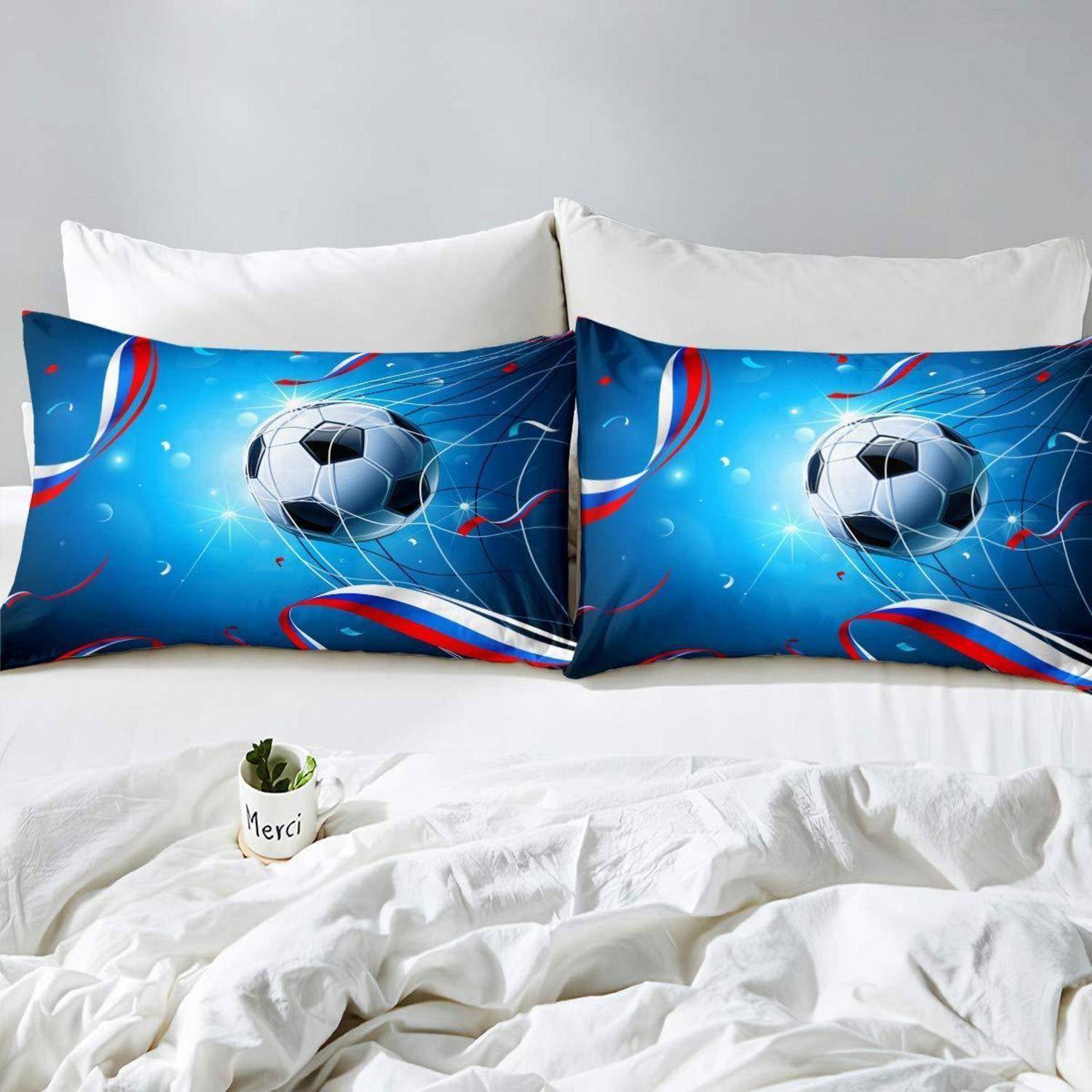 Zwei blaue Fußball-Themakissen zum Werfen mit einem Fußballdesign auf einem weißen Bett mit weißen Kissen und einer kleinen Topfpflanze.