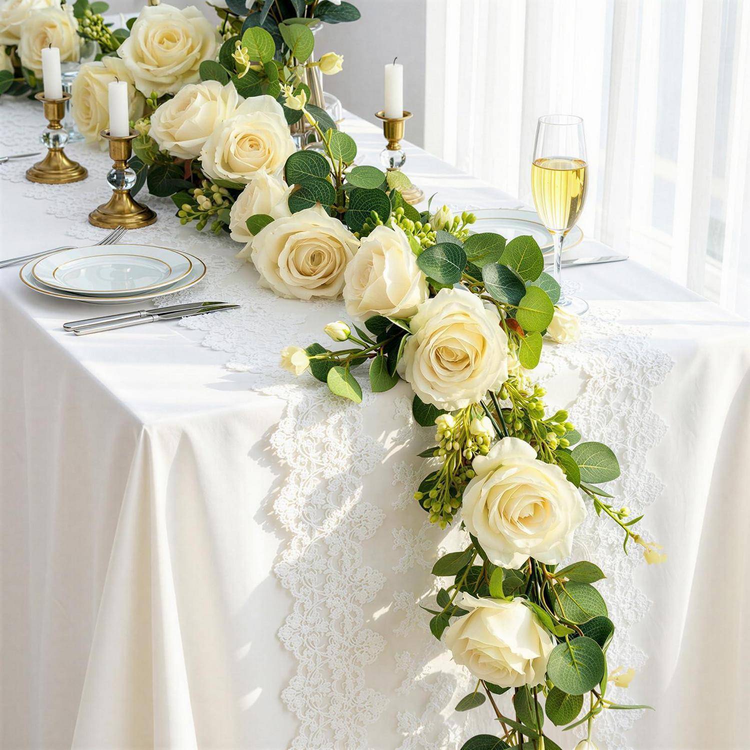 Weiße Rosen- und Grünpflanzen-Tischgirlande mit goldenen Kerzenleuchtern und Gedeck auf einem weißen Tisch, die eine elegante Hochzeitsempfang-Dekoration schaffen