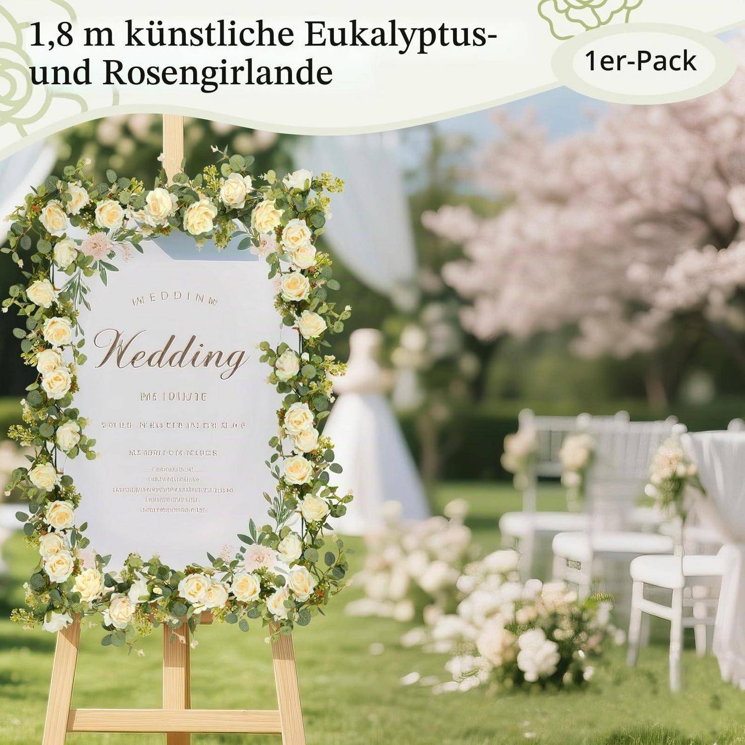 Hochzeitswillkommensschild auf einer Staffelei, umrahmt mit cremefarbenen Rosen und Eukalyptus bei einer Außentrauung; der Text lautet „Hochzeit".