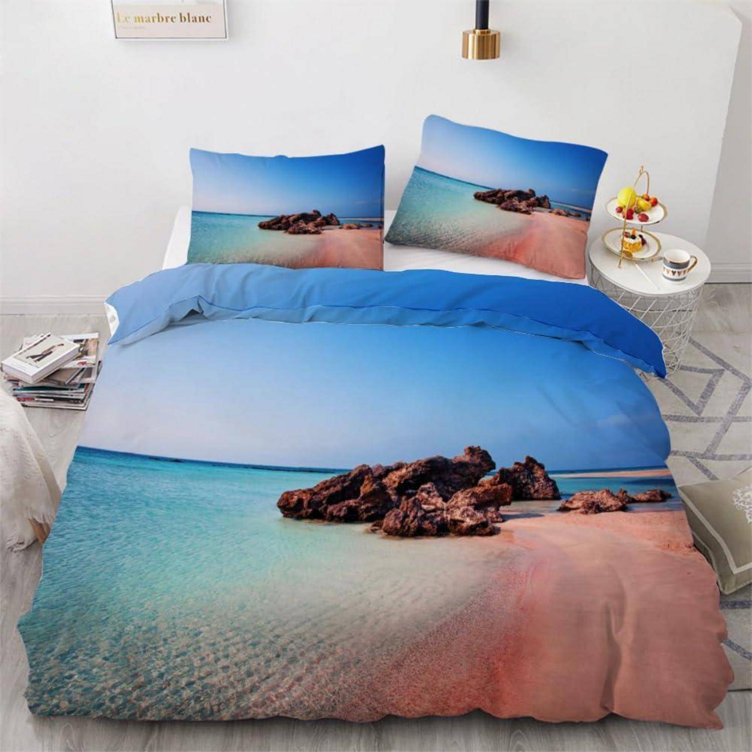 Bett mit Strandschlafzimmer-Bettwäscheset mit Meer-und-Felsen-Druck auf Bettdecke und Kissen in einem hellen Schlafzimmer.