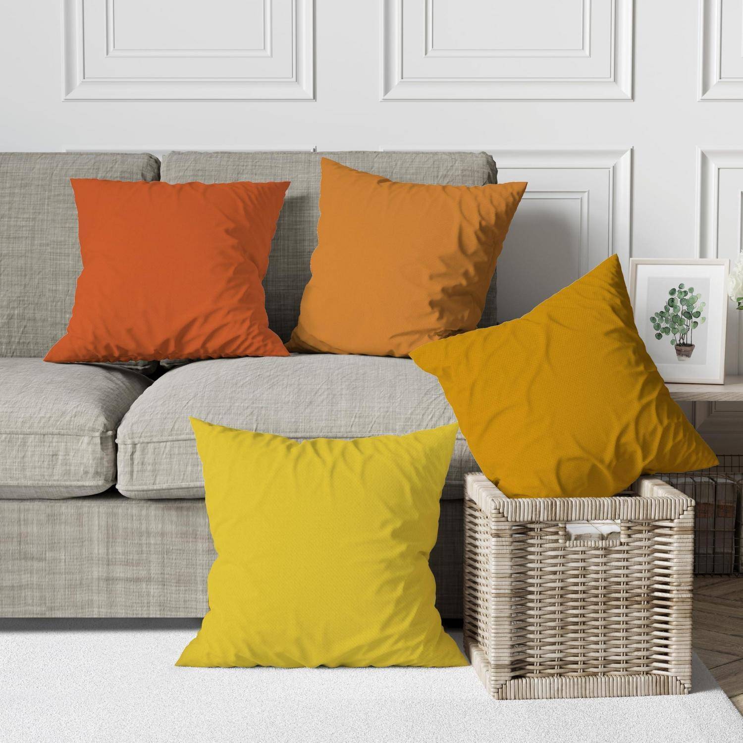 Graues Sofa mit vier bunten quadratischen Dekokissen in Orange, Senf und Gelb neben einem Weidenkorb und einem gerahmten Pflanzendruck.