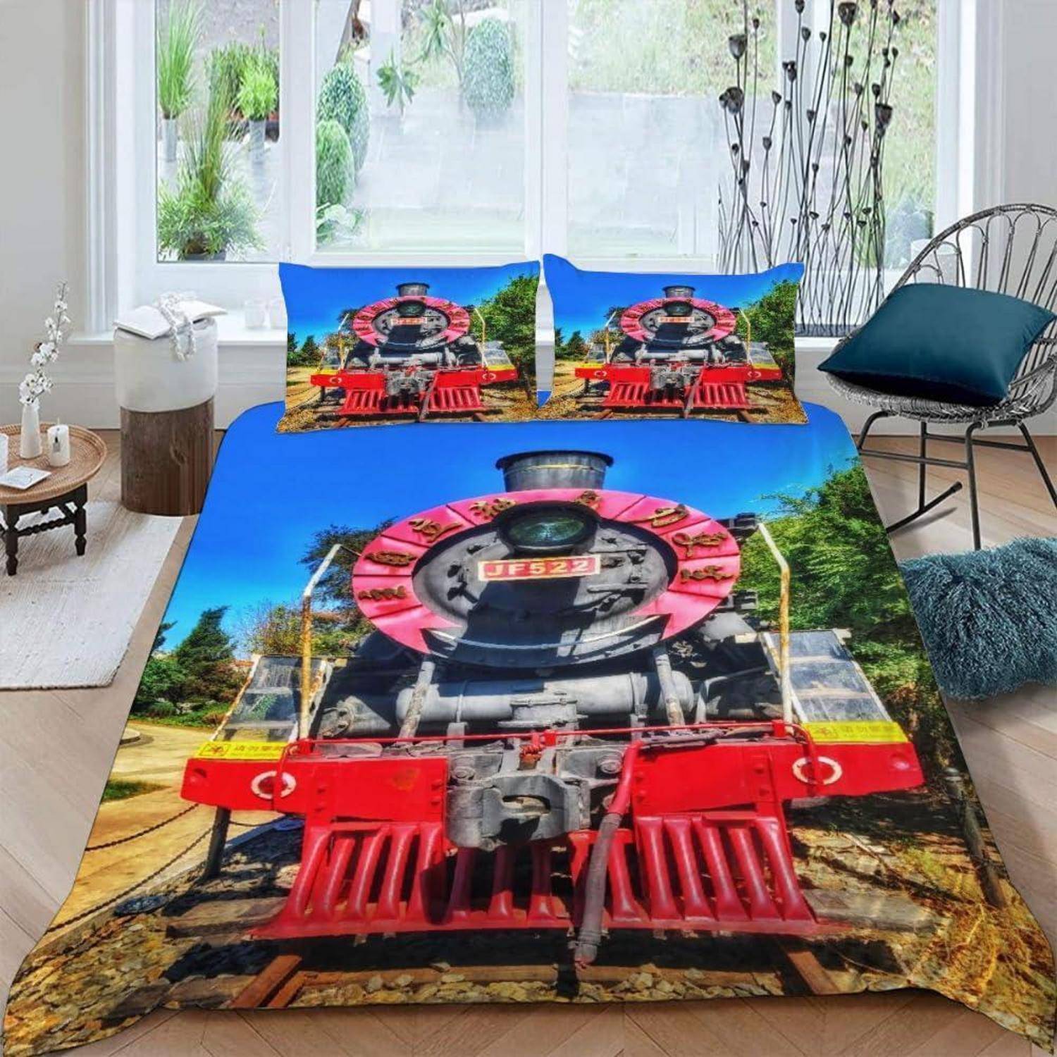 Ein Schlafzimmer mit einem Bett, das mit einer leuchtend farbigen Bettwäsche im Zugdesign ausgestattet ist, einschließlich eines großen Lokomotiv-Motivs auf dem Bettdecke und passenden Kissen.