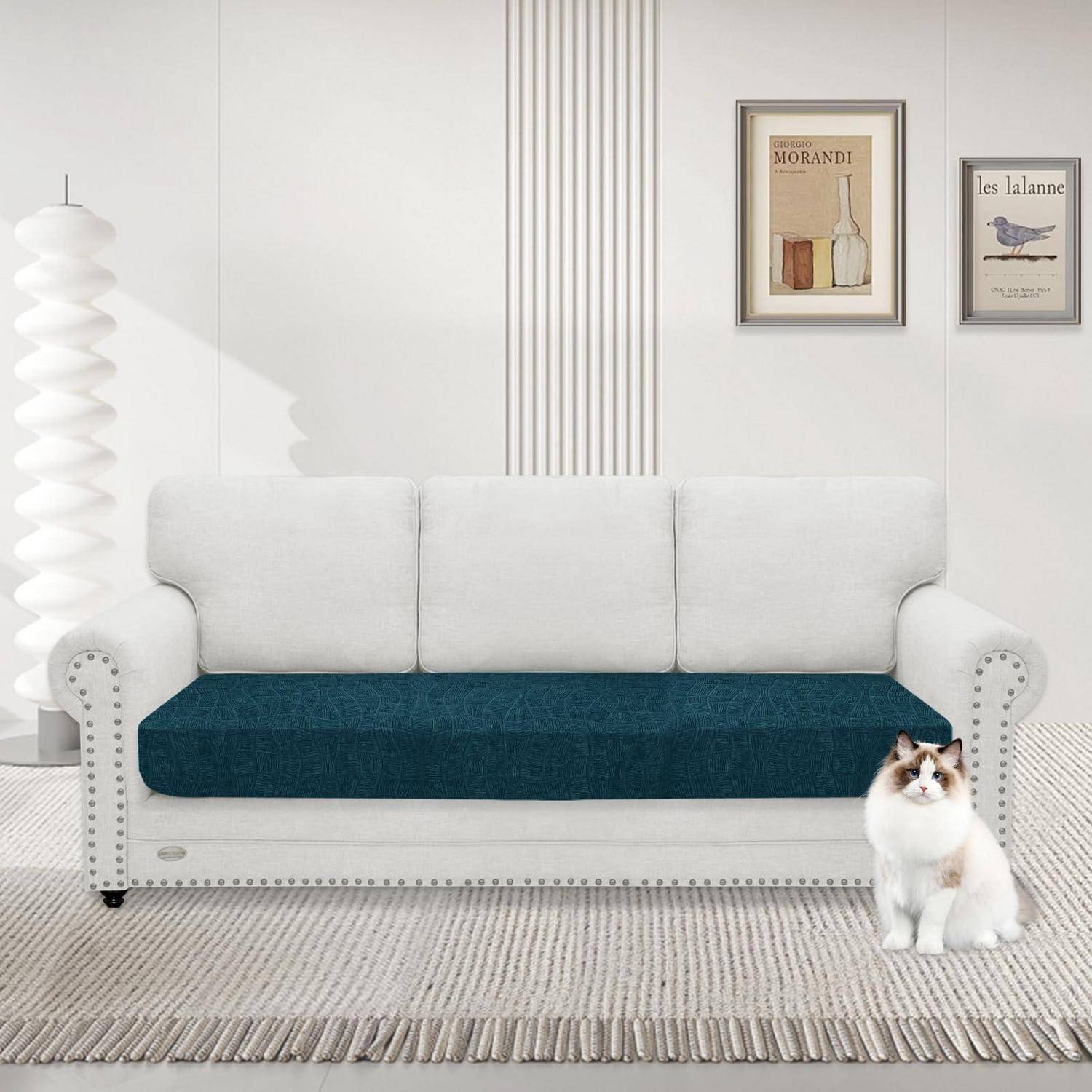 Weißes Sofa mit türkisem Sitzkissen in einem minimalistischen Wohnzimmer, mit einer Katze, die auf dem Teppich daneben sitzt, und gerahmter Wandkunst darüber.