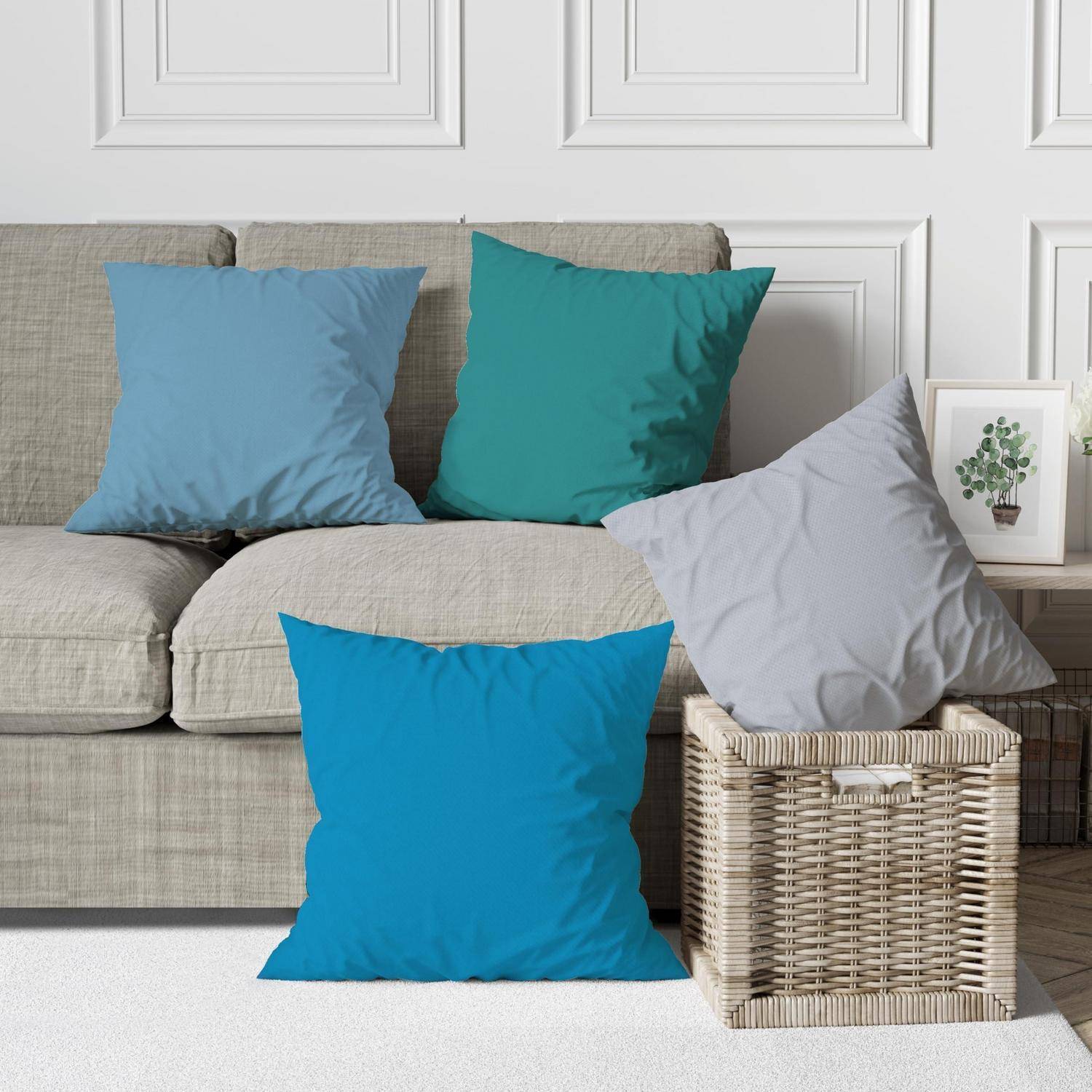 Fünf bunte Dekokissen, die auf einem beigen Sofa arrangiert sind, und ein Weidenkorb in einem hellen Wohnzimmer.